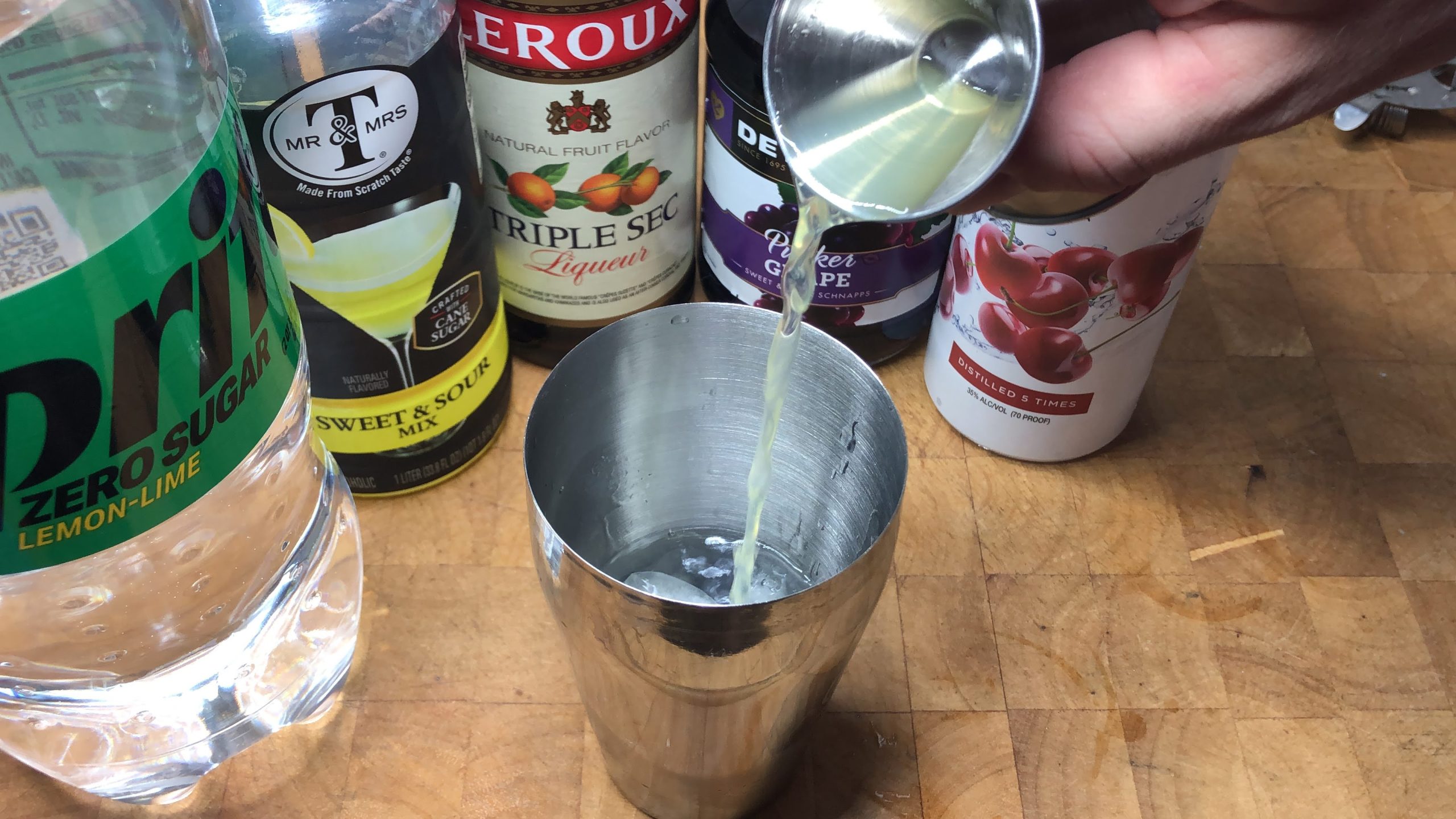 Pouring sweet and sour mix from a jigger into a cocktail shaker.