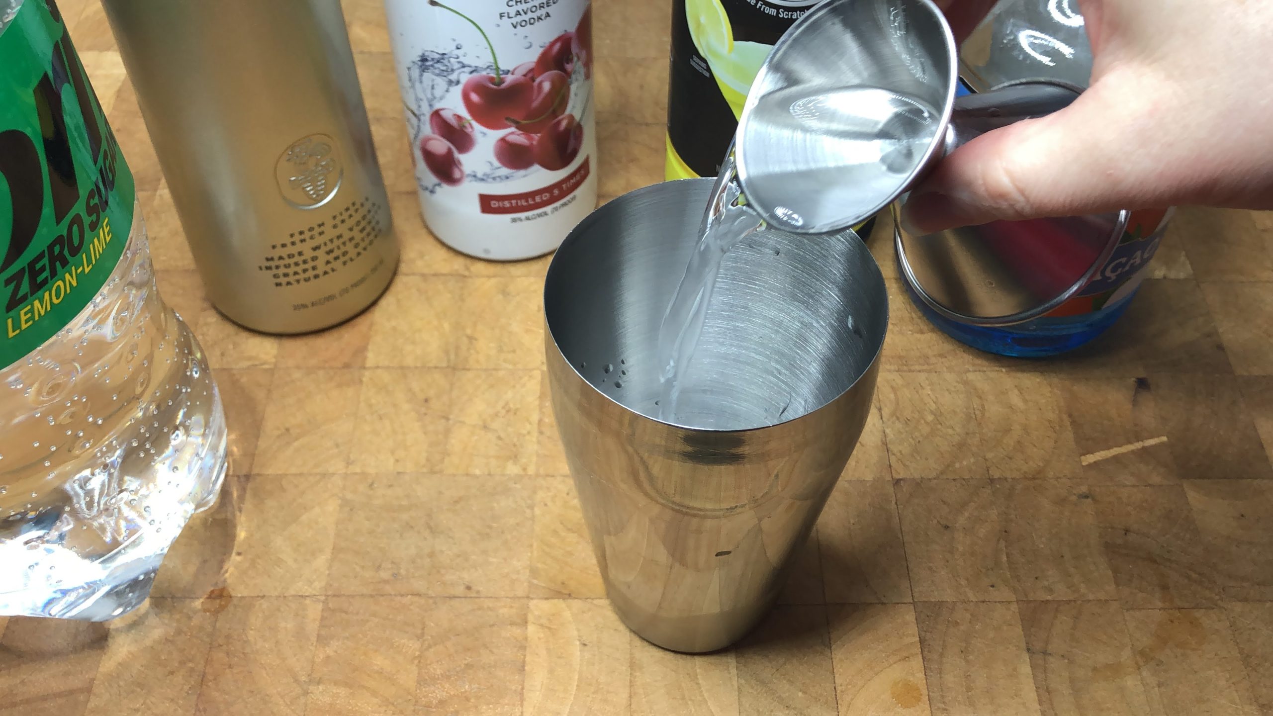 Pouring cherry vodka from jigger into cocktail shaker.