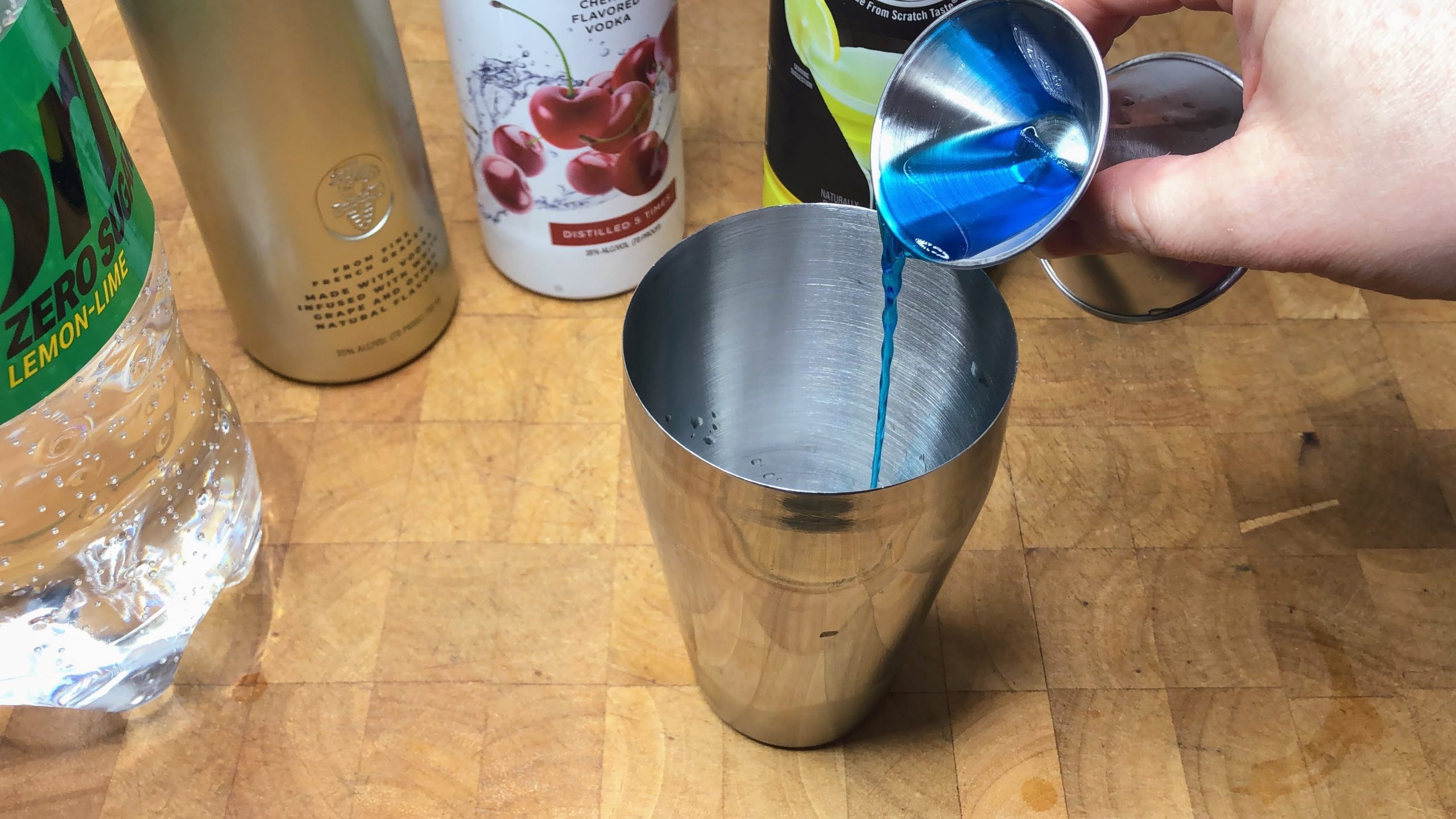 Pouring blue curacao from a jigger into a cocktail shaker.