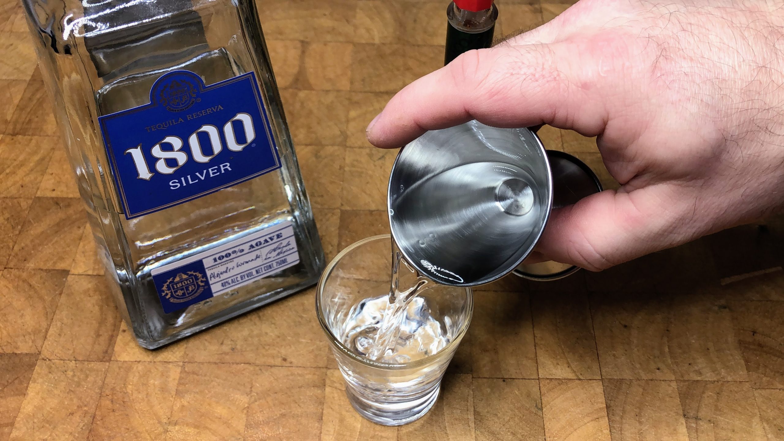 Pouring tequila from jigger into a shot glass.