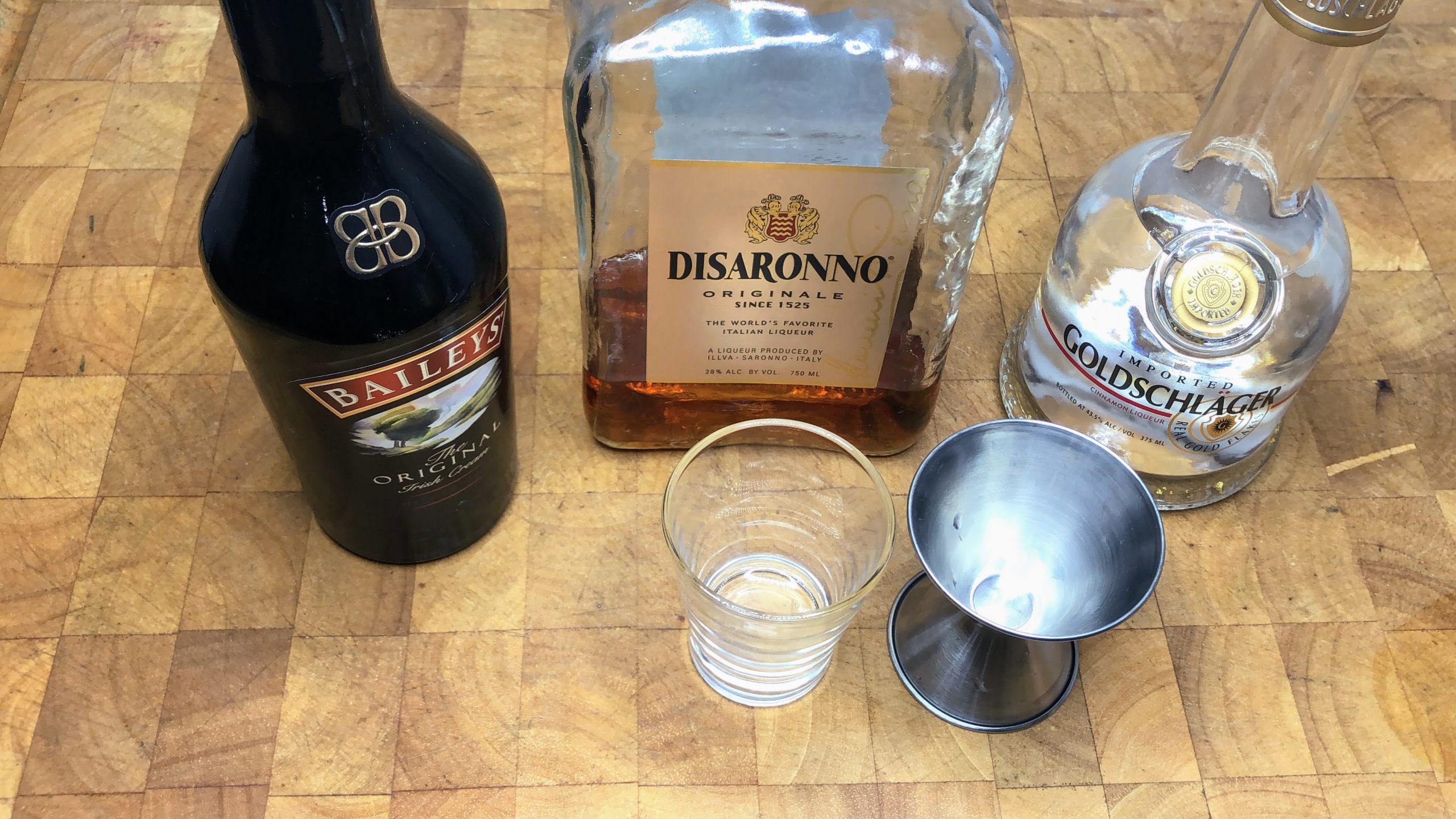 Jigger next to an empty shot glass, goldschlager, irish cream, and amaretto.