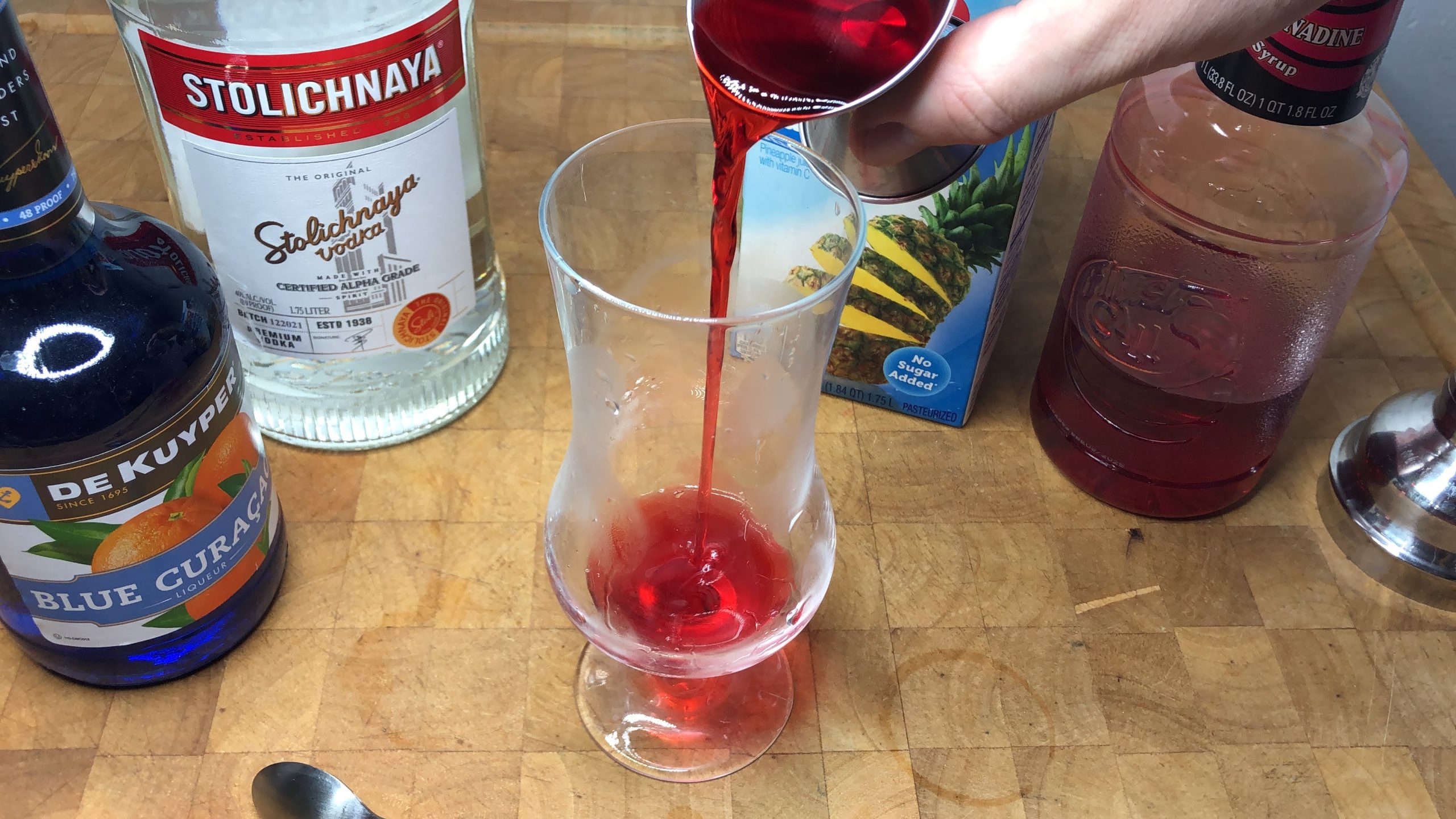 Pouring grenadine from a jigger into a hurricane glass.