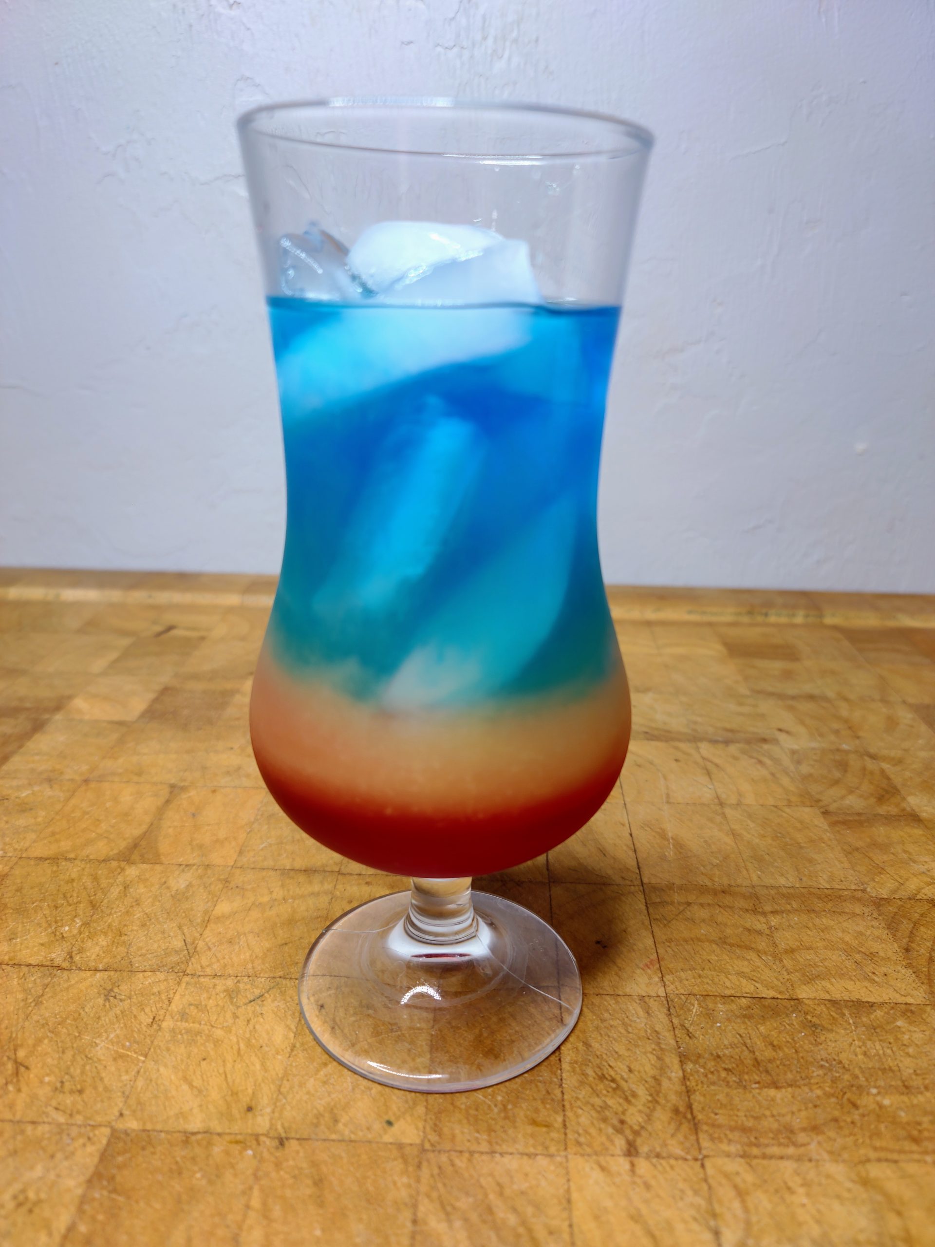 Rainbow cocktail in a hurricane glass on a wooden table.