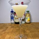 Raspberry lemon drop martini on a wooden table in front of ingredient bottles.