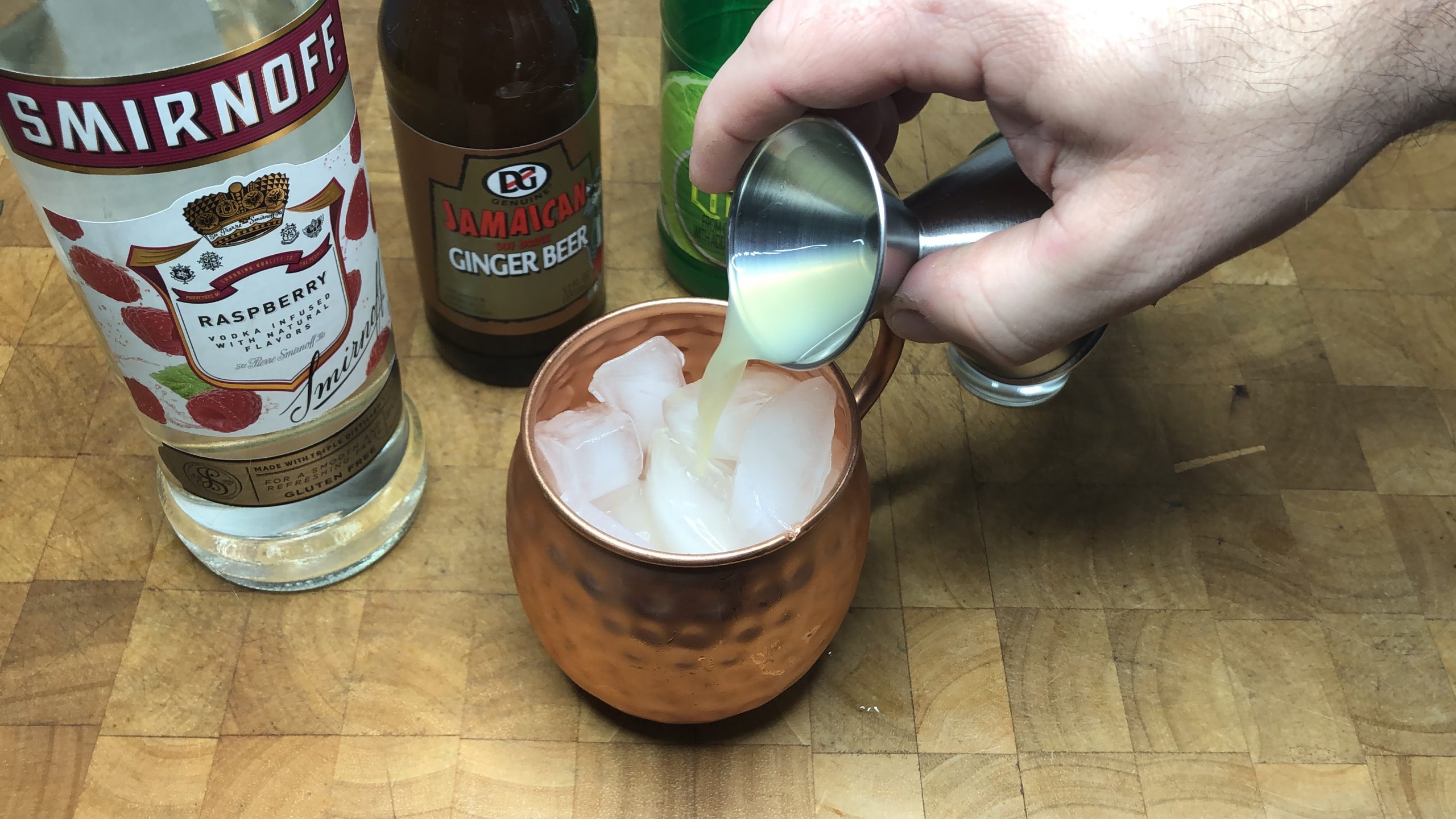 Pouring lime juice from a jigger into a mug.
