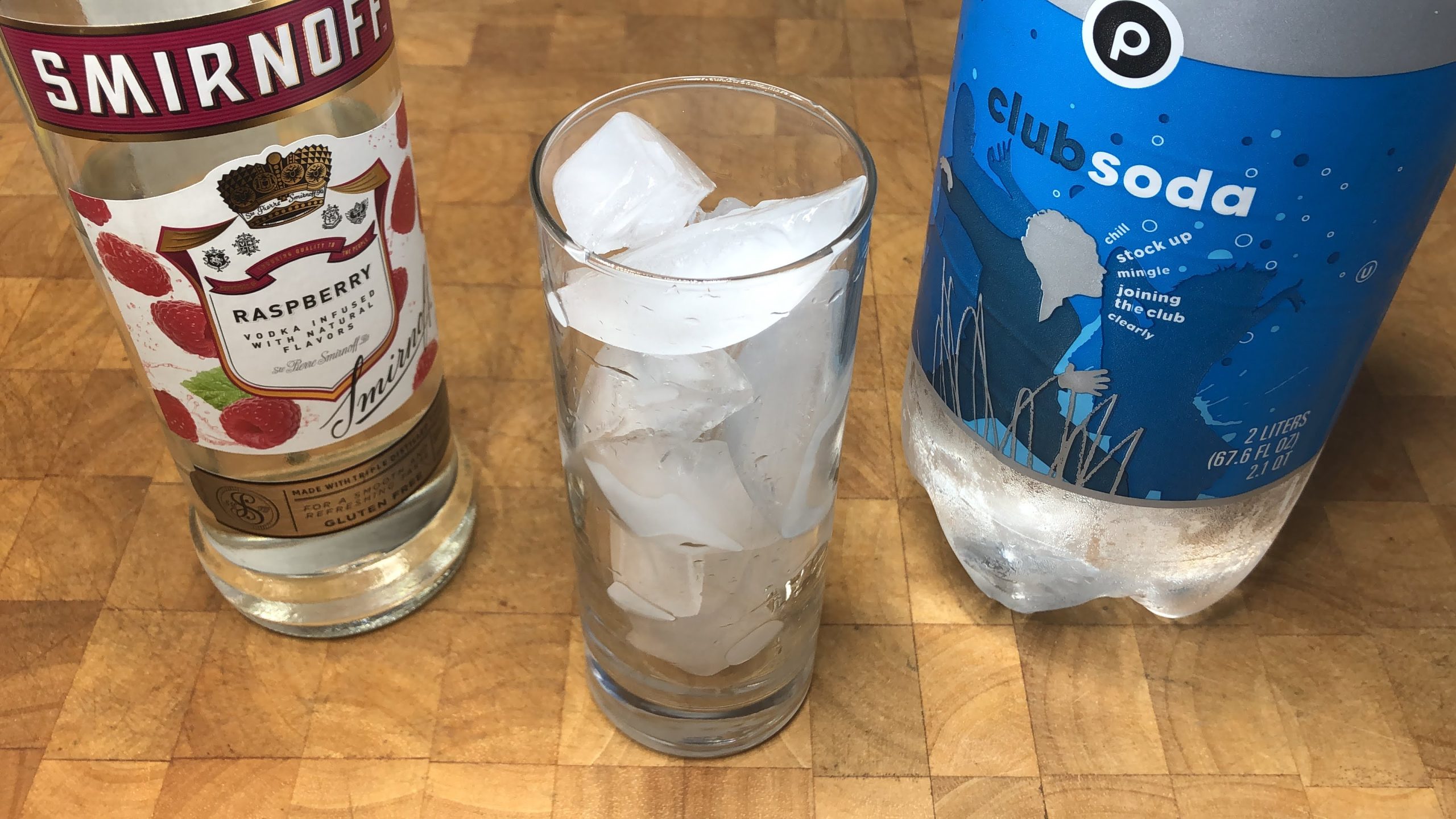 Highball glass filled with ice next to club soda and raspberry vodka.