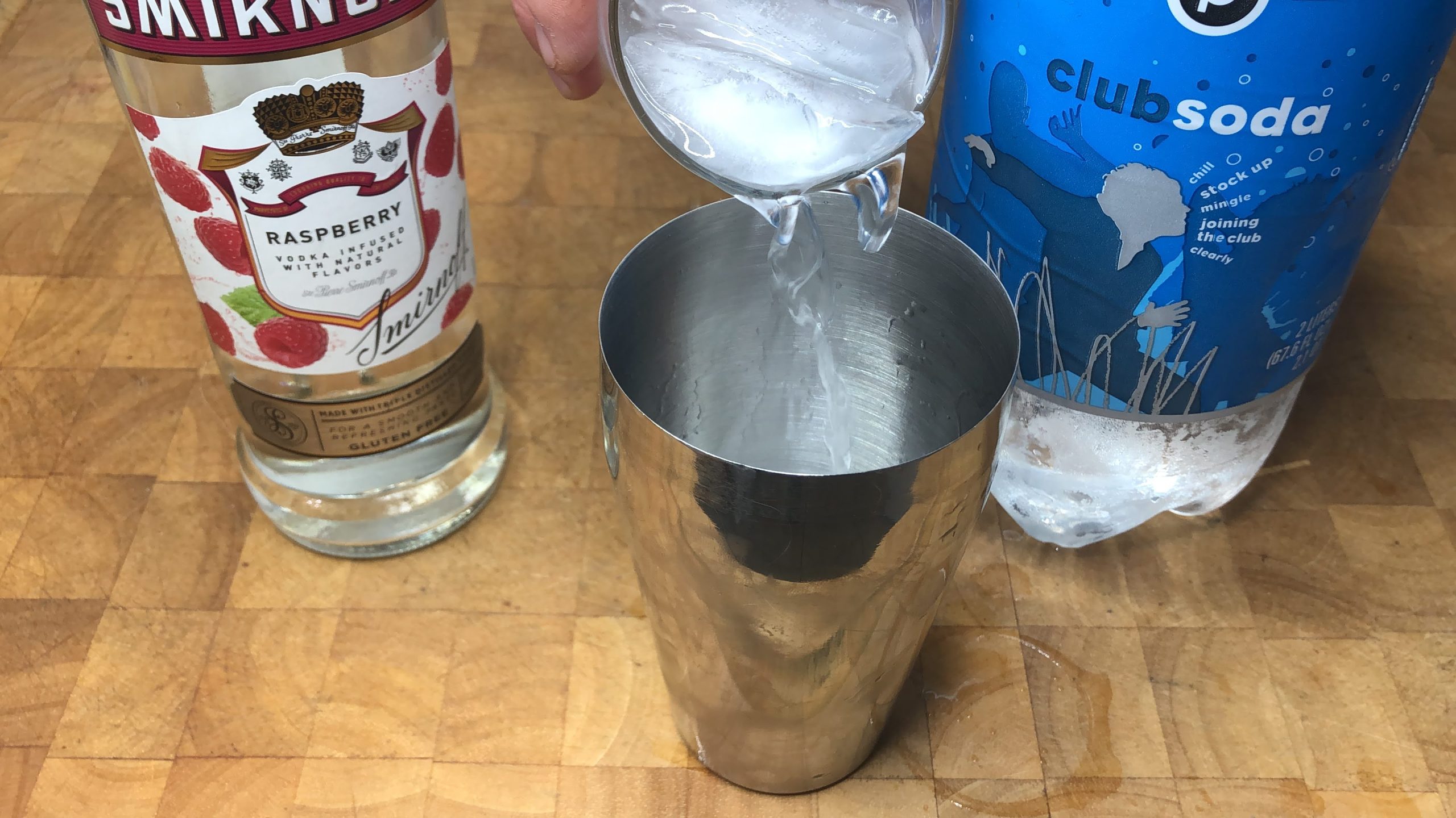 Pouring raspberry vodka soda from a glass into a cocktail shaker.