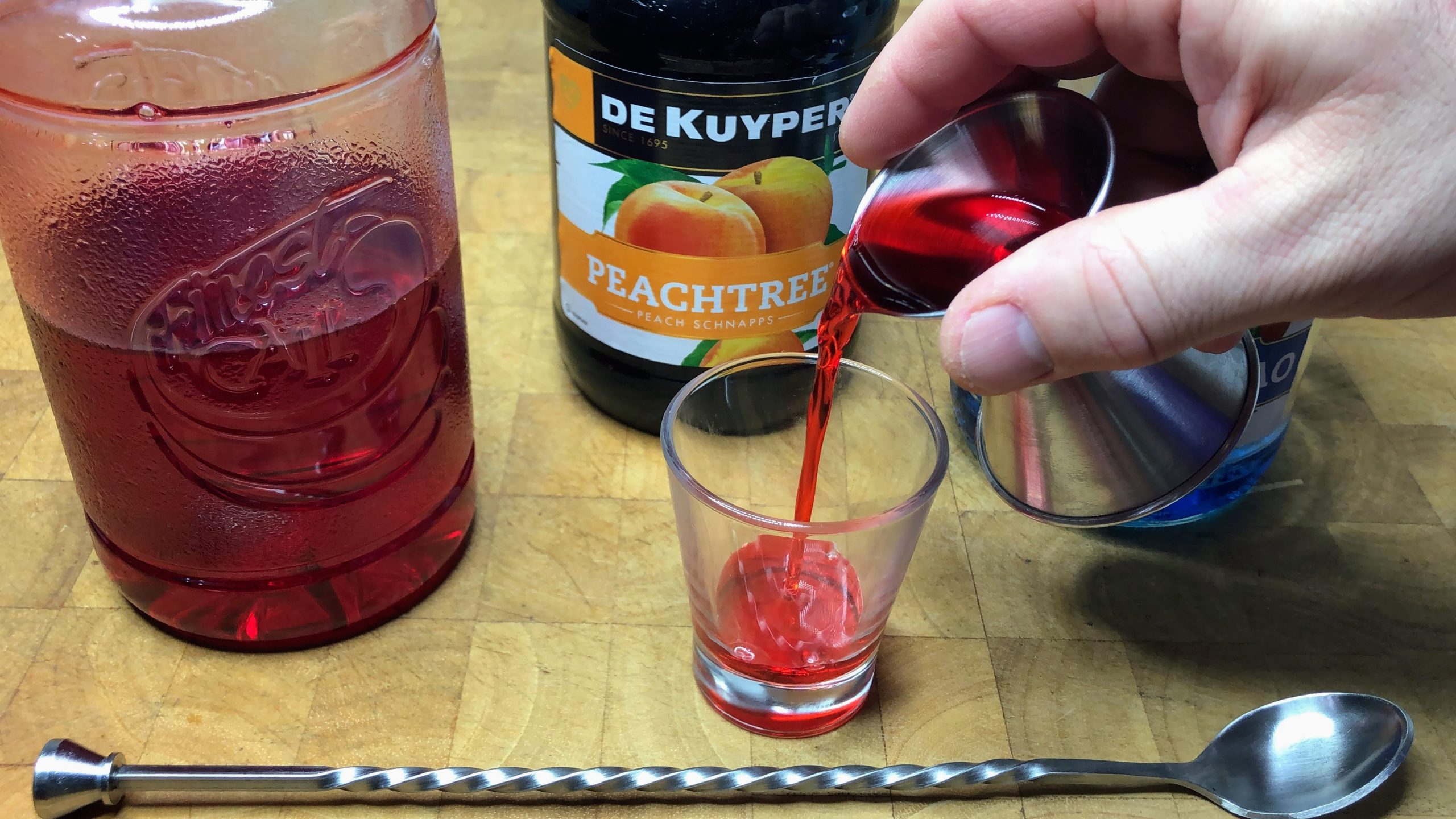 Pouring grenadine from a jigger into a shot glass.
