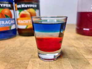Red, white and blue shot with ingredient bottles around the shot glass.