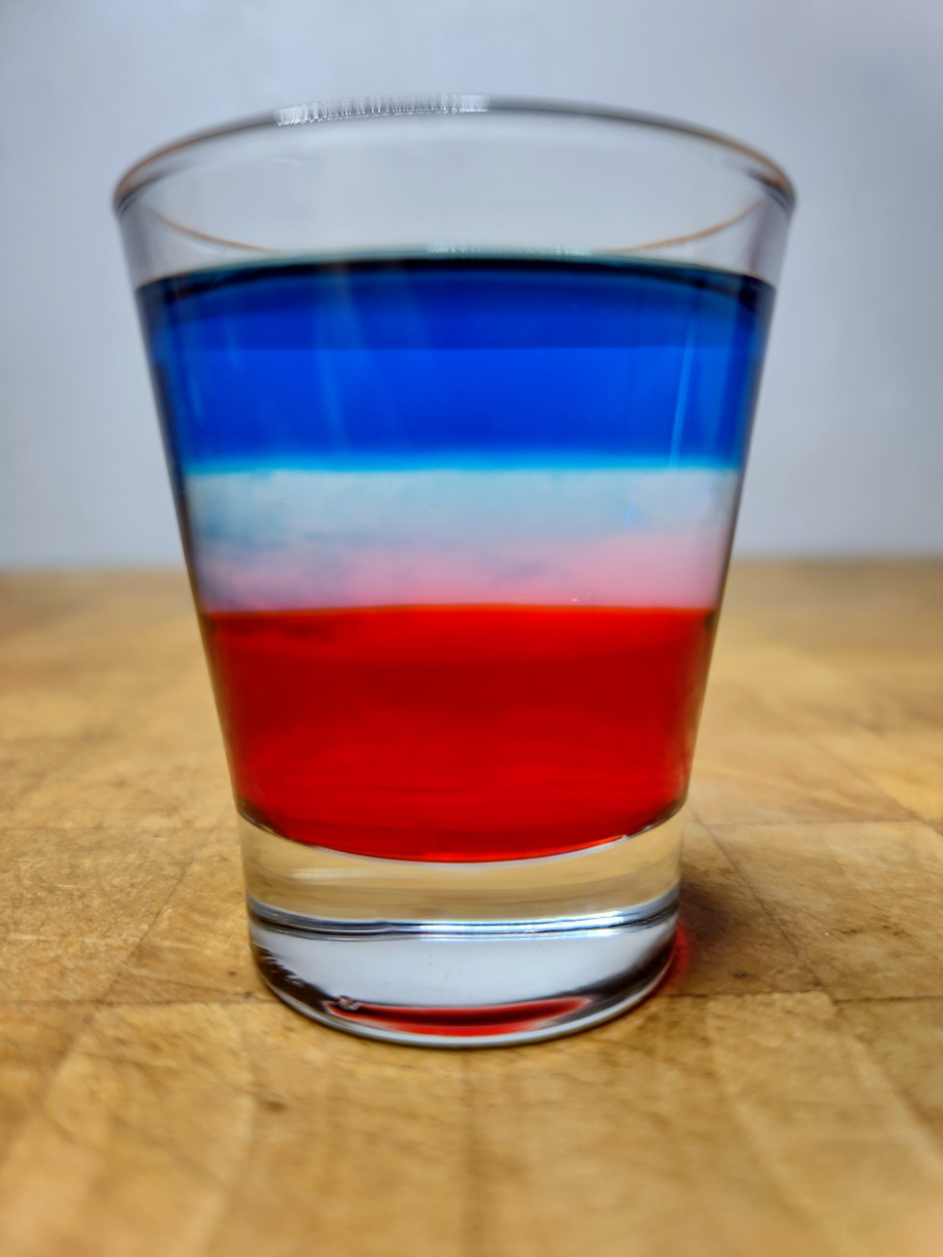 Closeup of a red, white and blue shot on a wooden table.