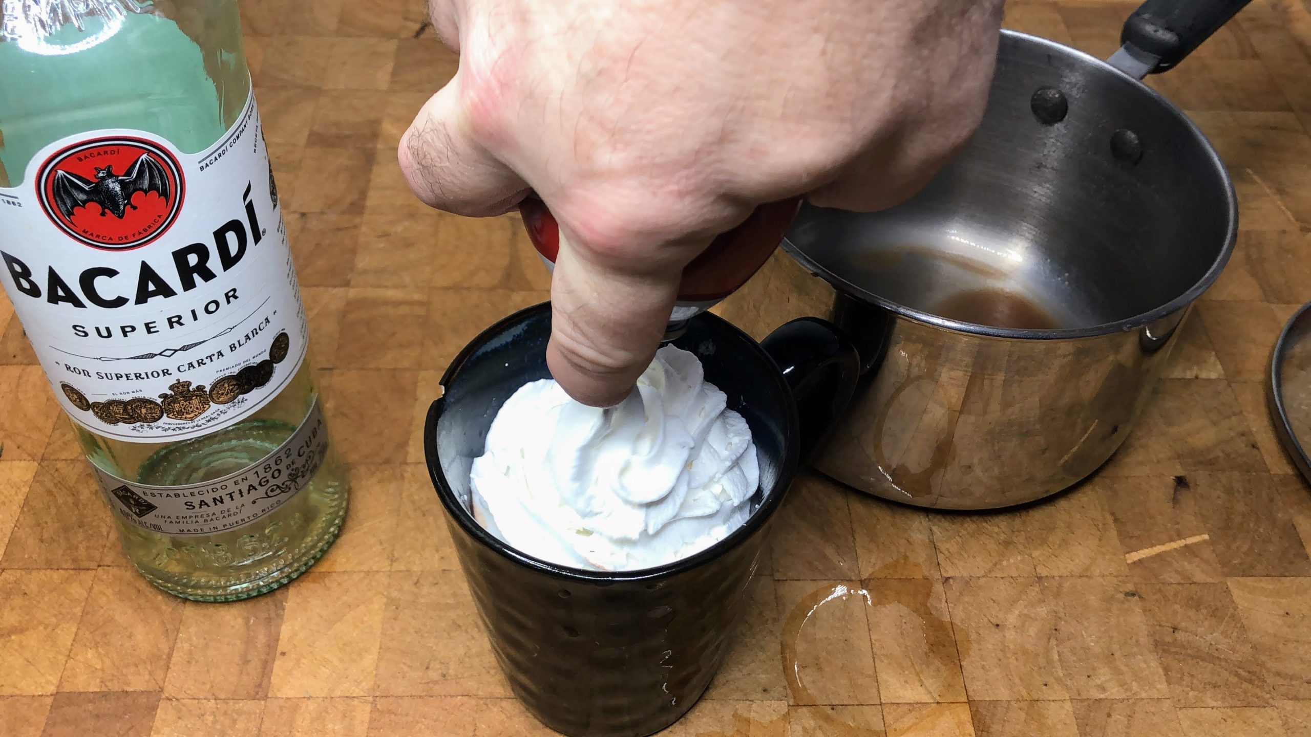Adding whipped cream to the top of rum hot chocolate.