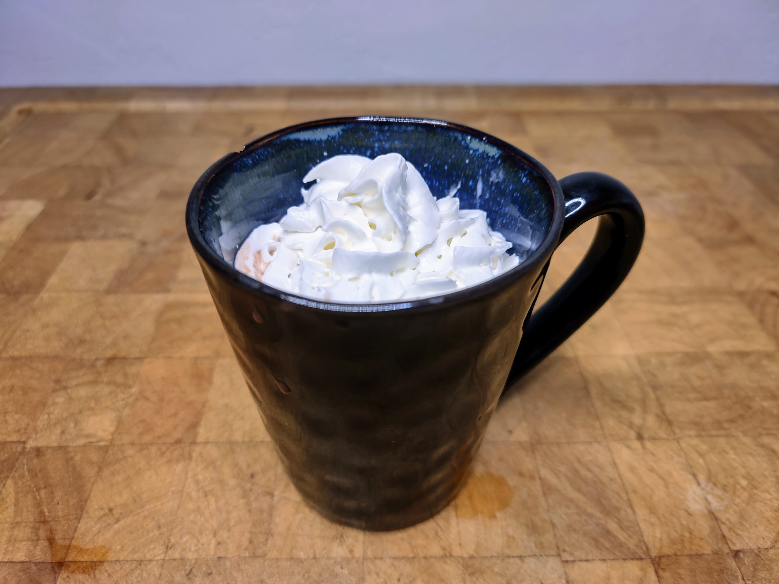 Rum hot chocolate in a blue mug topped with whipped cream on a wooden table.
