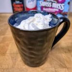 Rumplemintz hot chocolate in a mug topped with whipped cream with ingredients behind the mug.