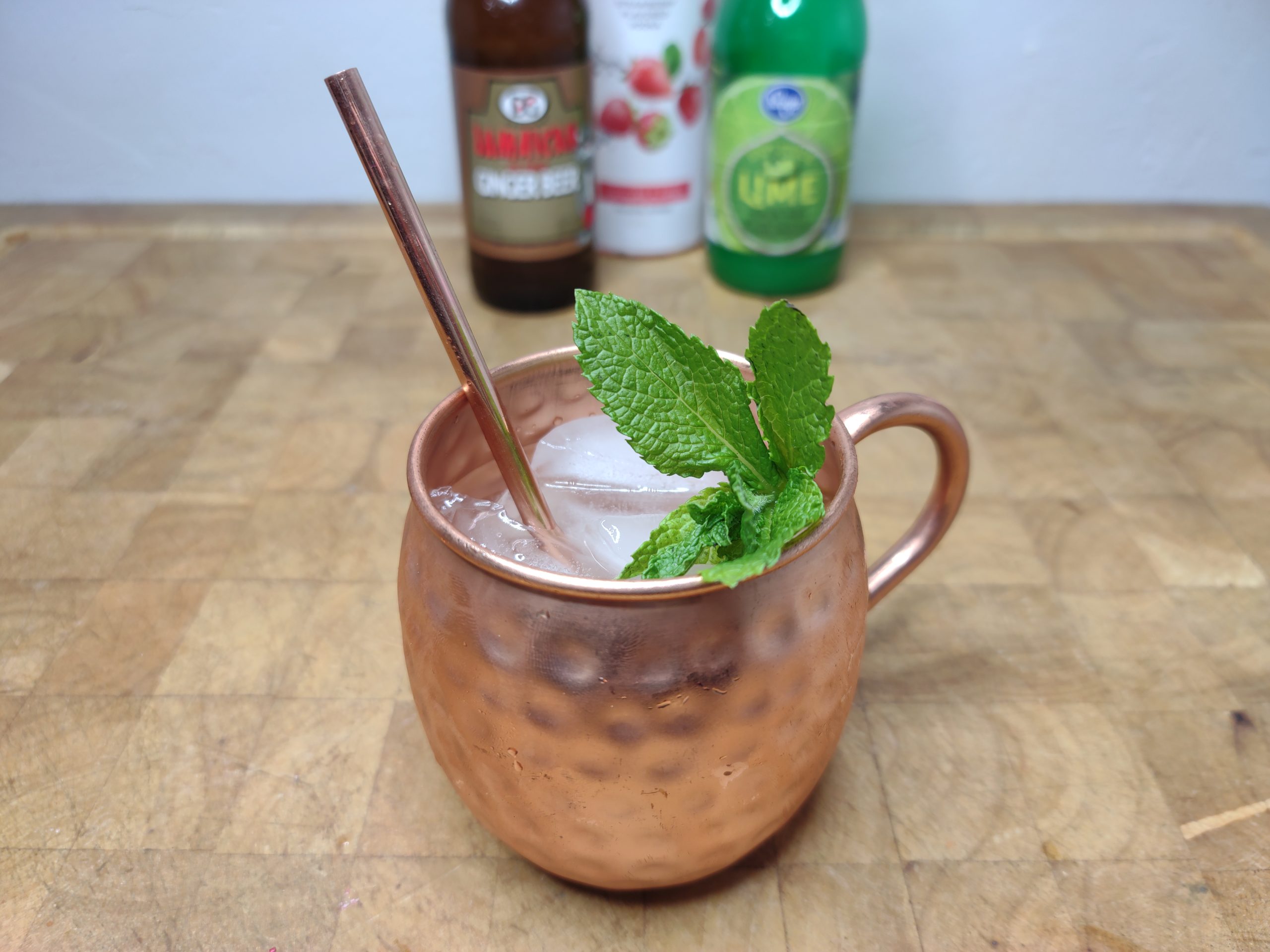 strawberry moscow mule in a copper mug with mint in the mug.  ingredient bottles in the background.