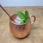 Strawberry moscow mule with copper straw and mint in mug on a wooden table.