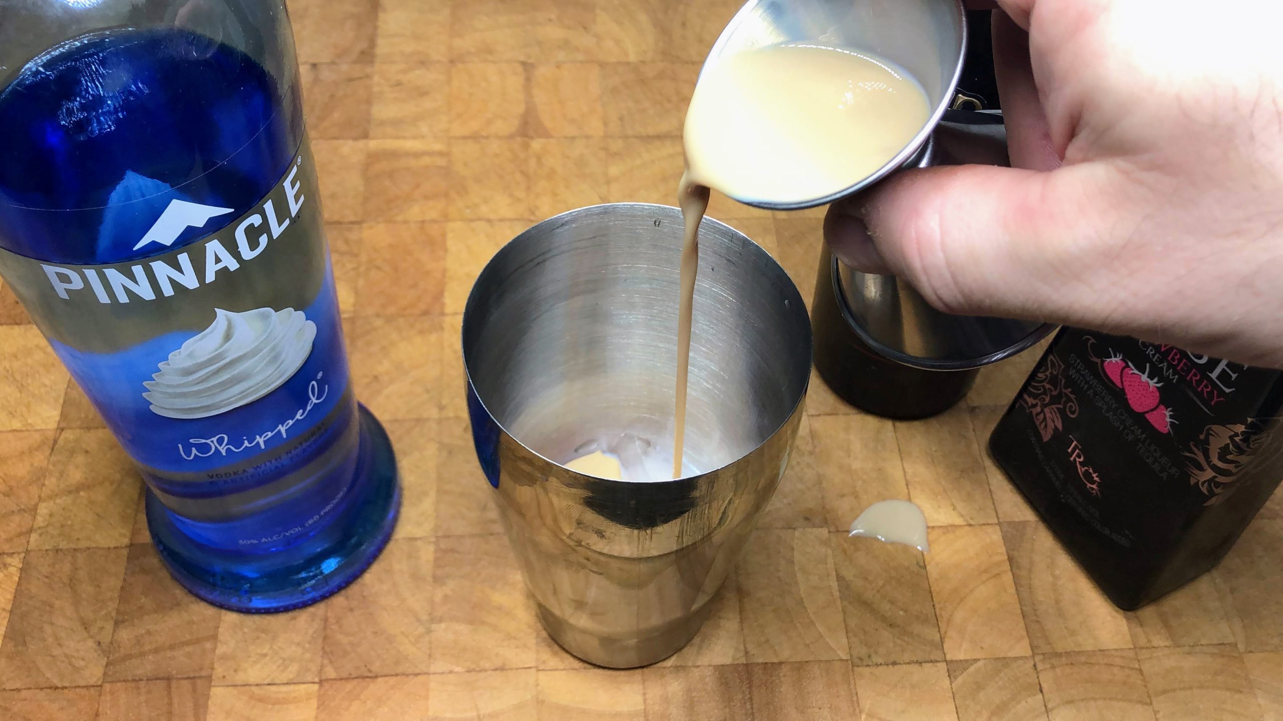Pouring irish cream from a jigger into a shaker.