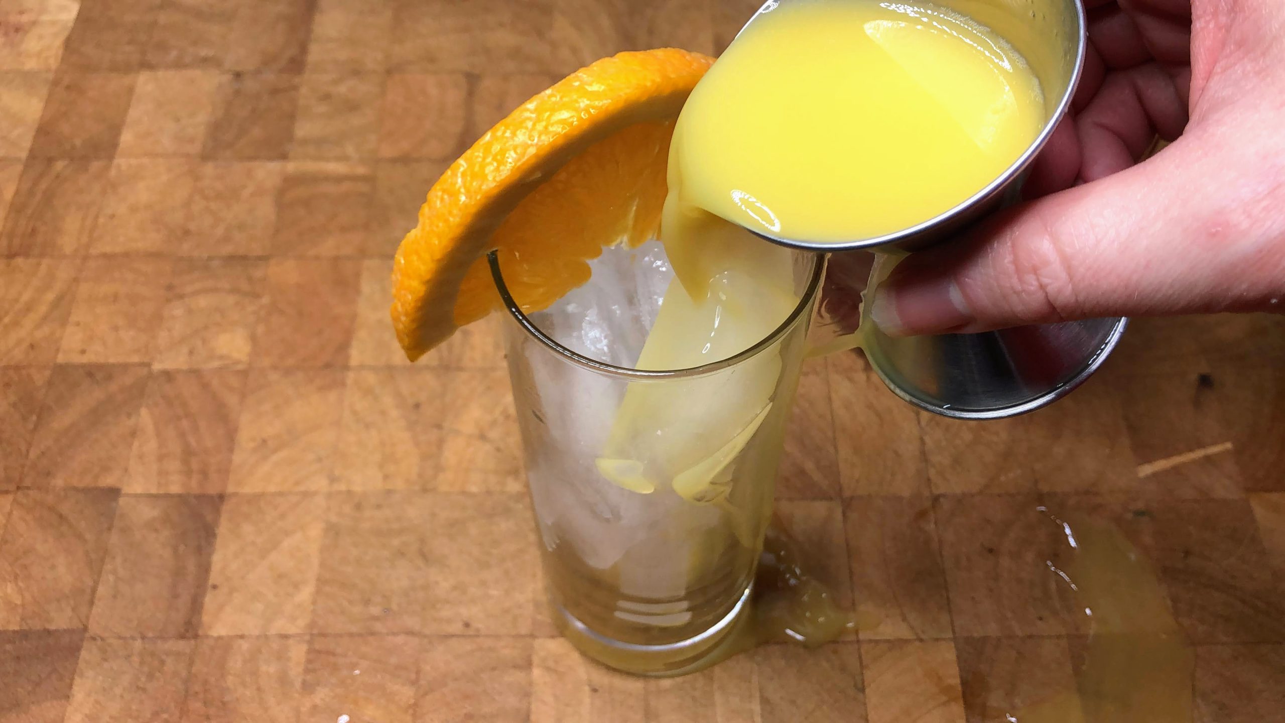 Pouring orange juice from a jigger into a highball glass.