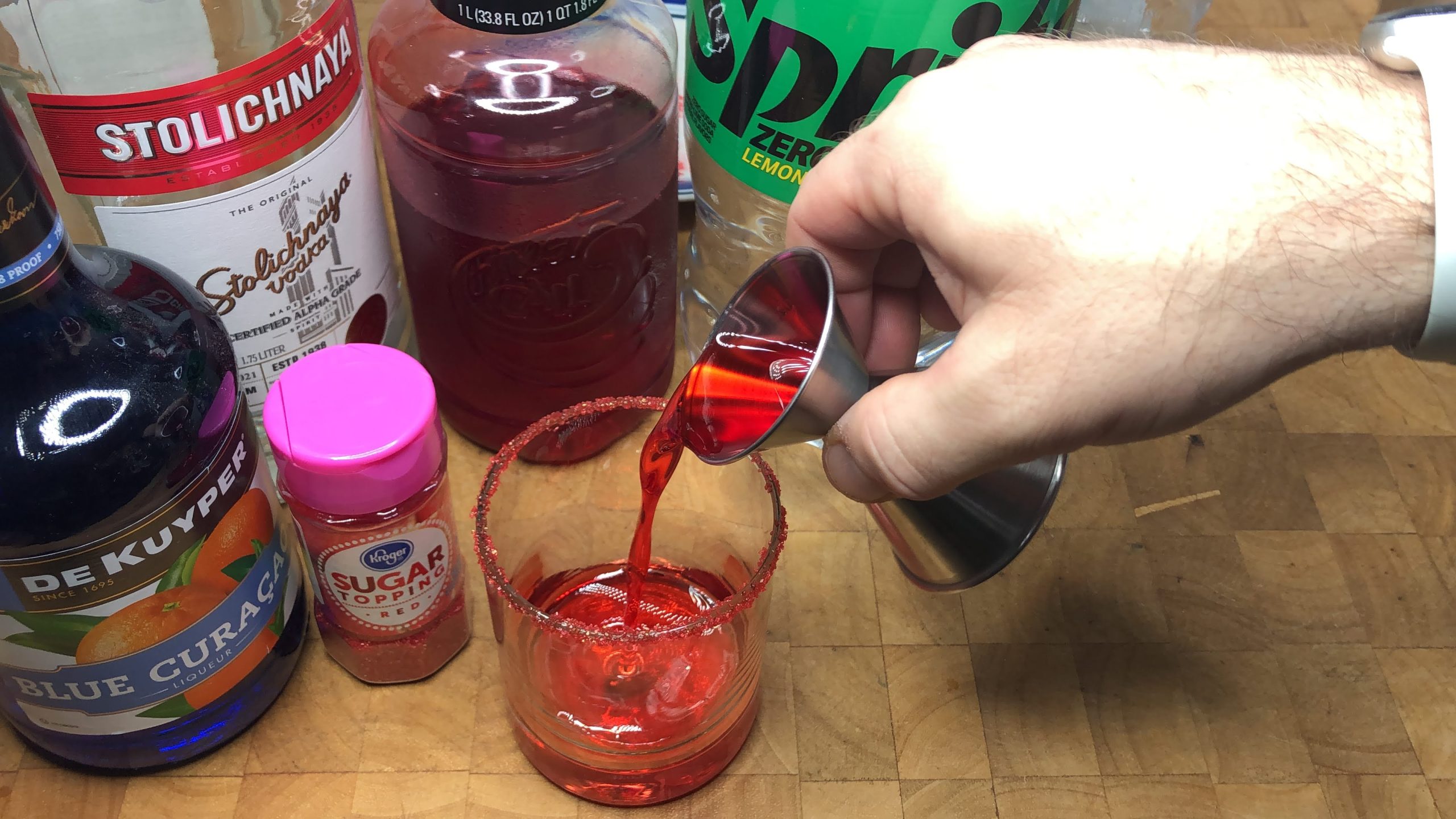 Pouring grenadine from a jigger into a rocks glass.