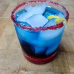 superman cocktail in a rocks glass with red sugar rim and a lemon twist on a wooden table.
