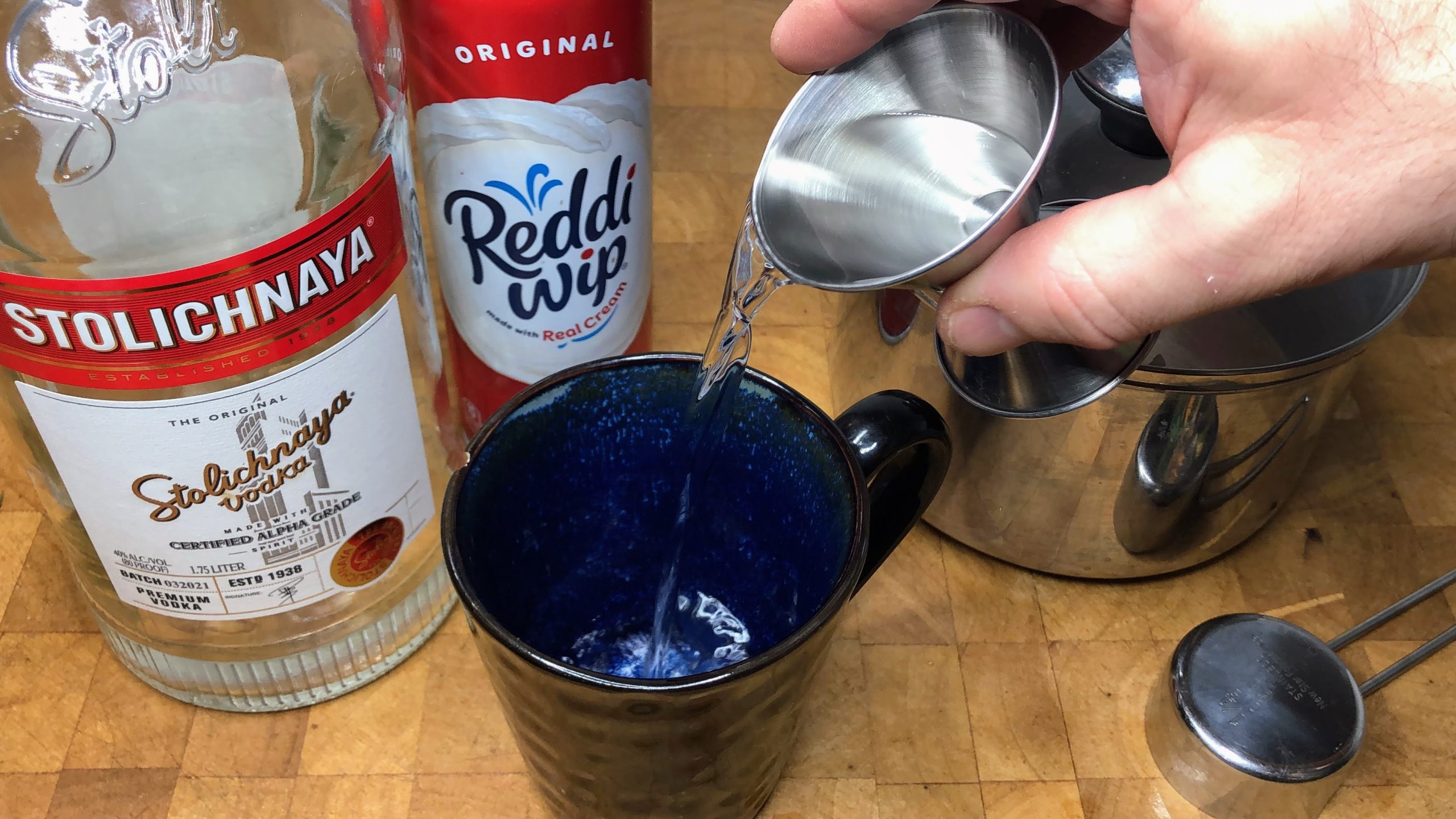Pouring vodka from jigger into a mug.