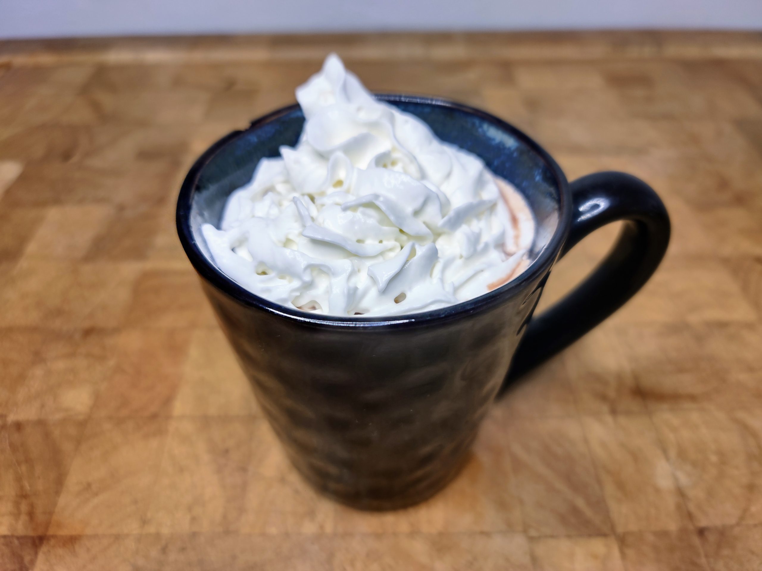 Vodka hot chocolate topped with whipped cream in a blue mug on a wooden table.