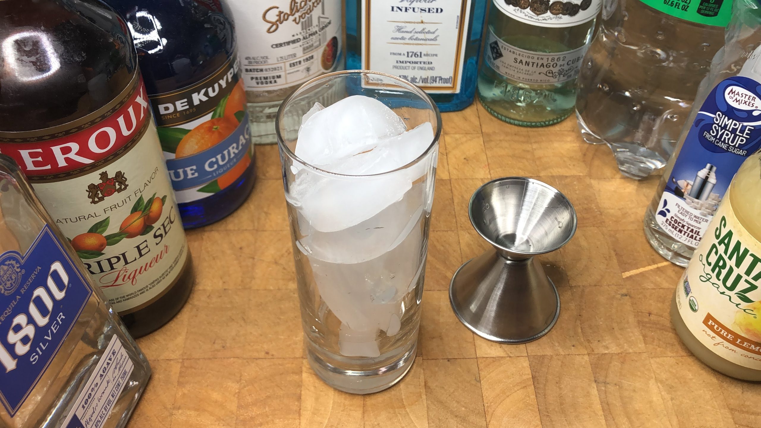 All the ingredients for the drink surrounding a jigger and highball glass with ice.