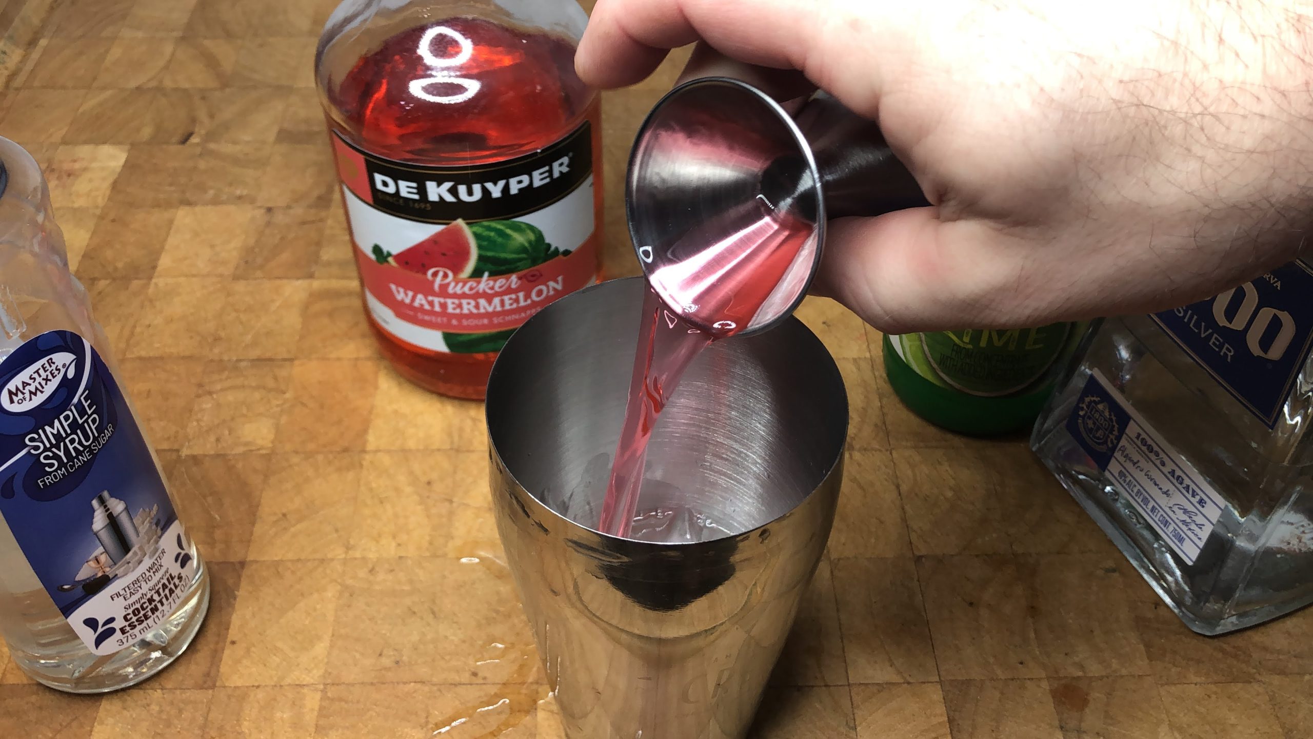 Pouring watermelon pucker from a jigger into a shaker.