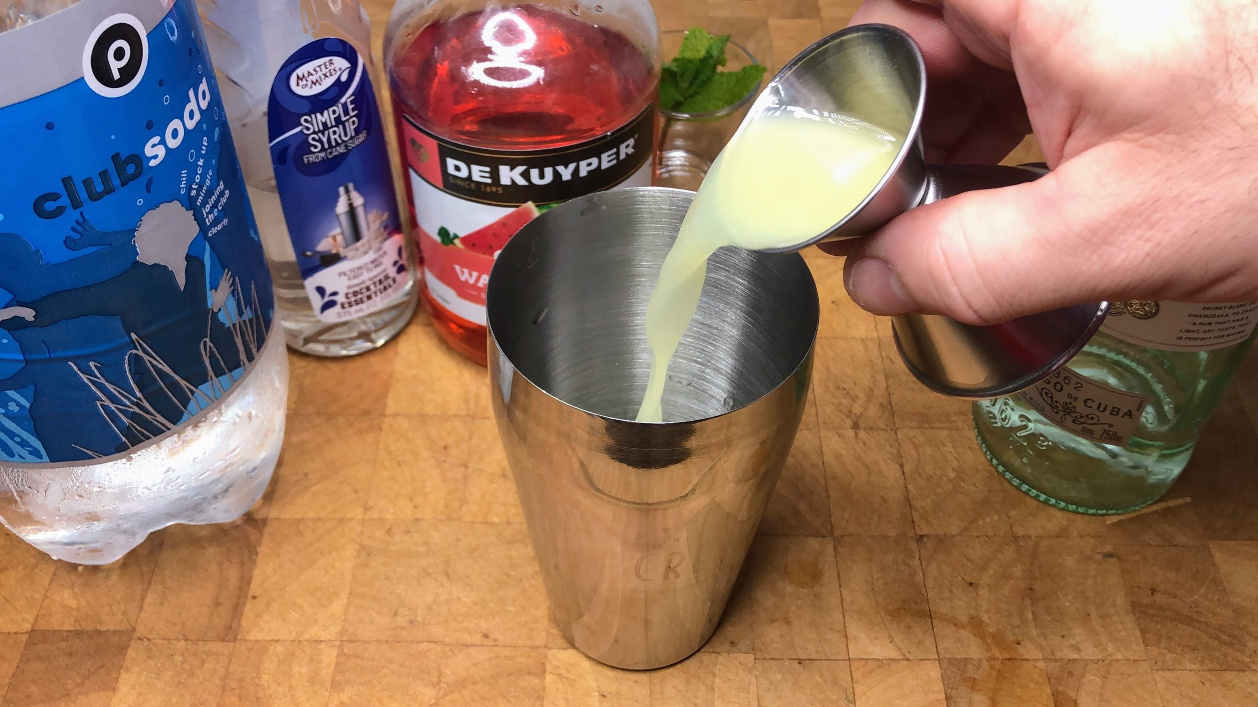 Pouring lime juice from the jigger into the shaker.