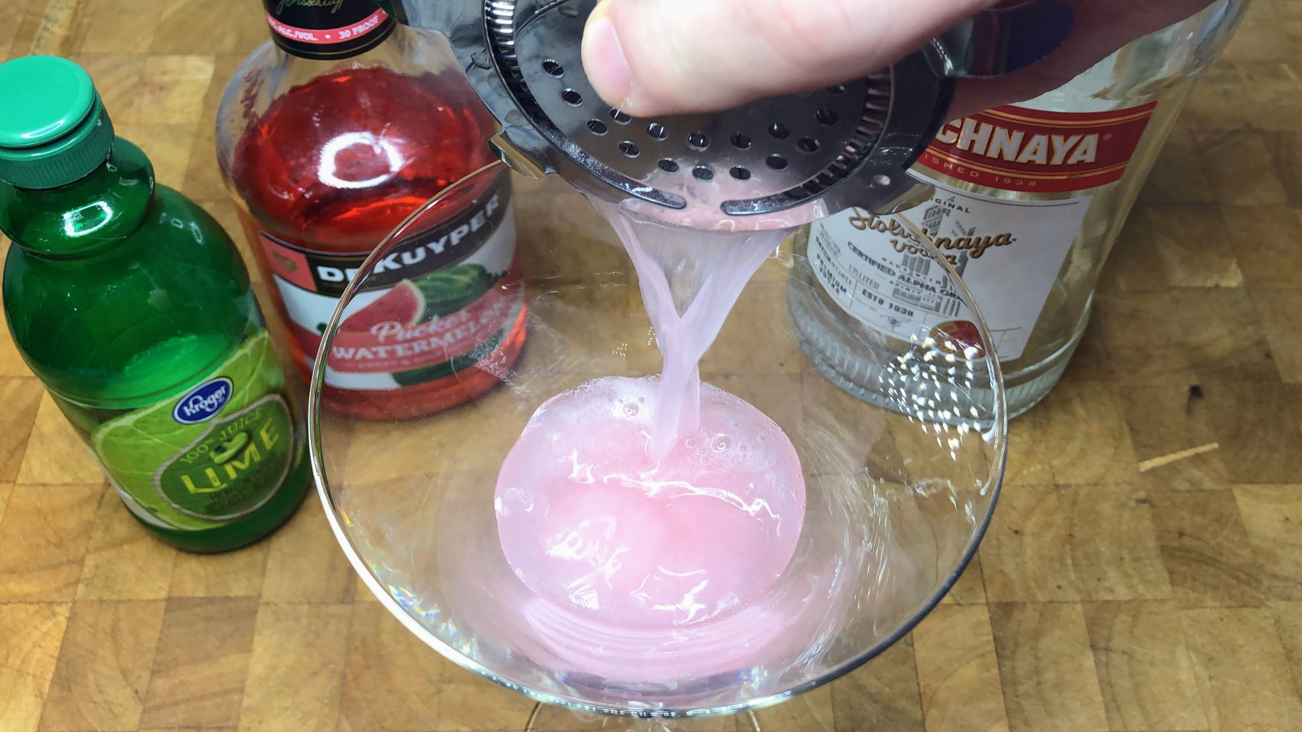 Straining watermelon pucker martini from shaker into glass.