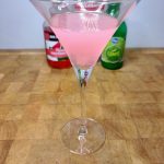 Watermelon pucker martini on a wooden table with ingredients in the background.