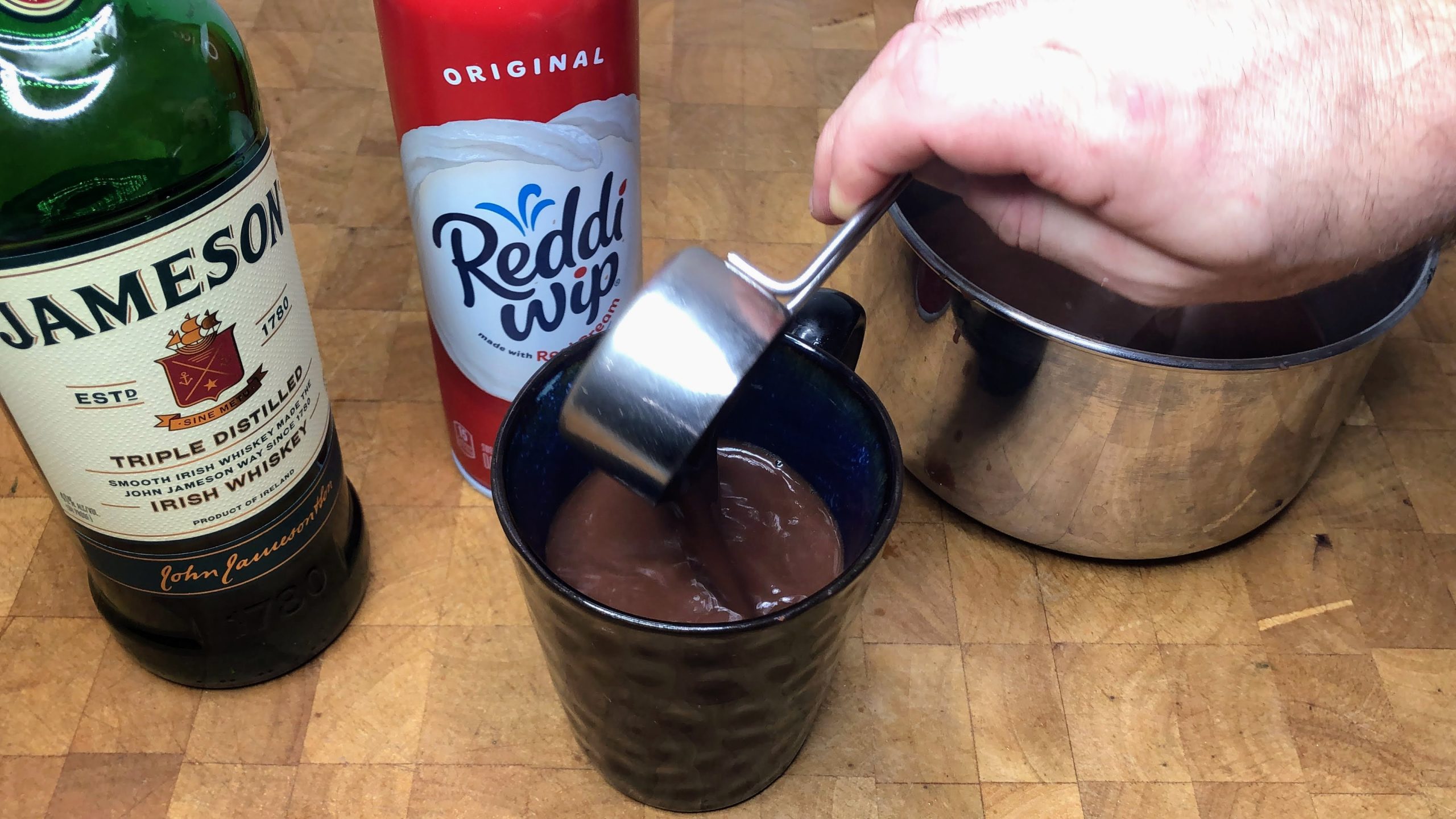 Pouring hot chocolate from measuring cup into a mug.