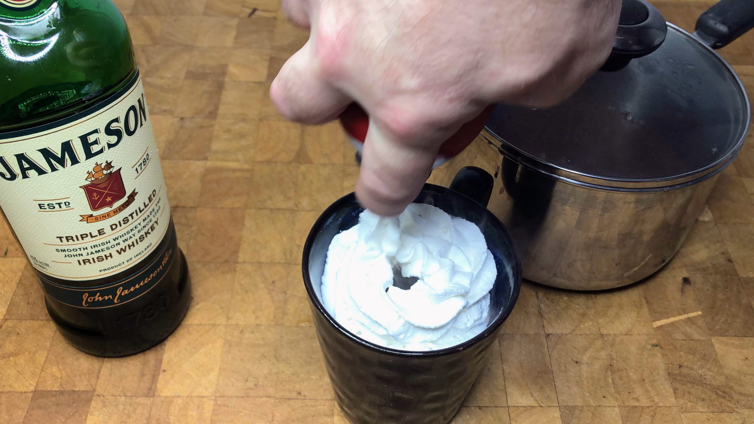 Squirting whipped cream on top of a whiskey hot chocolate.