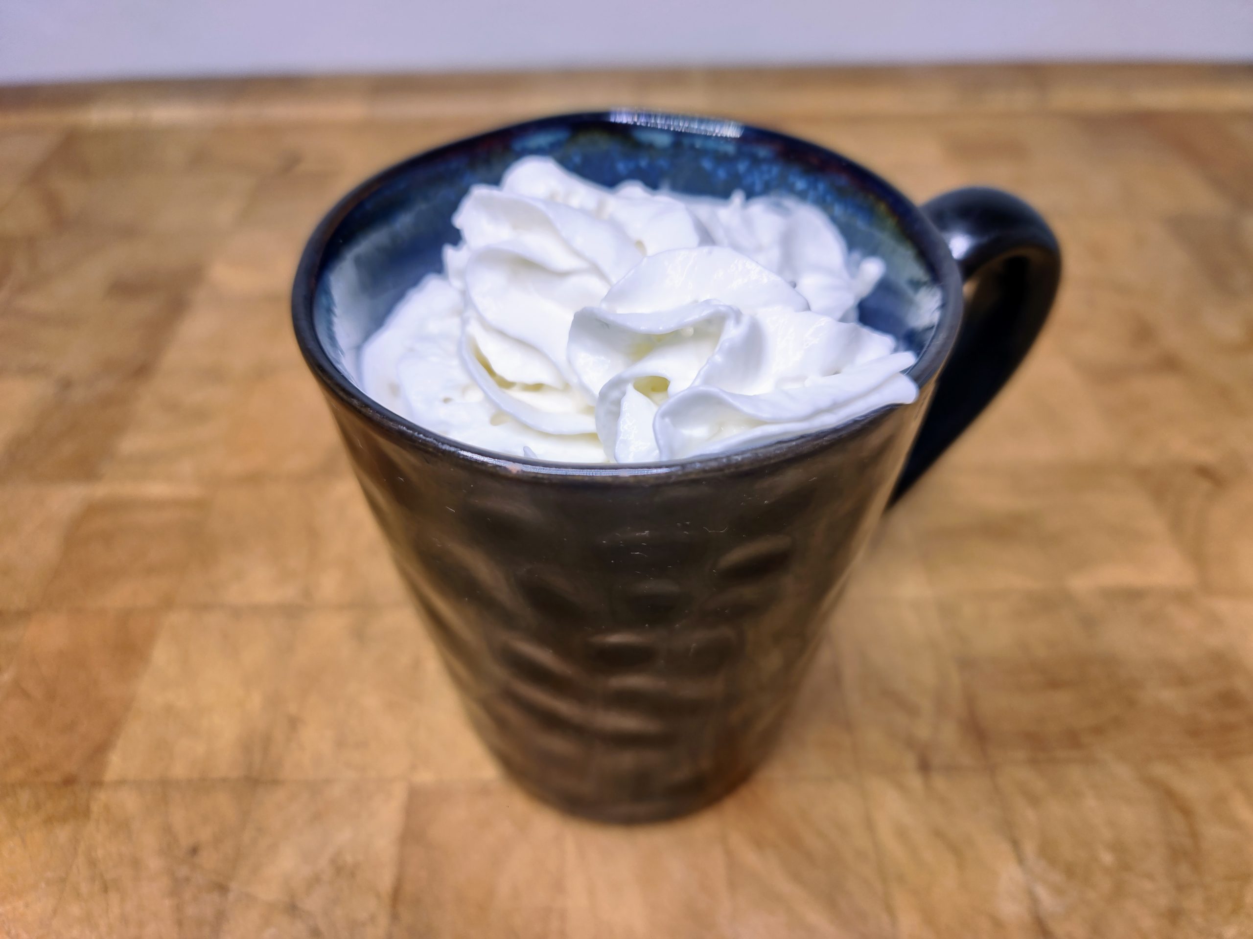 Whiskey hot chocolate in a mug topped with whipped cream on a wooden table.