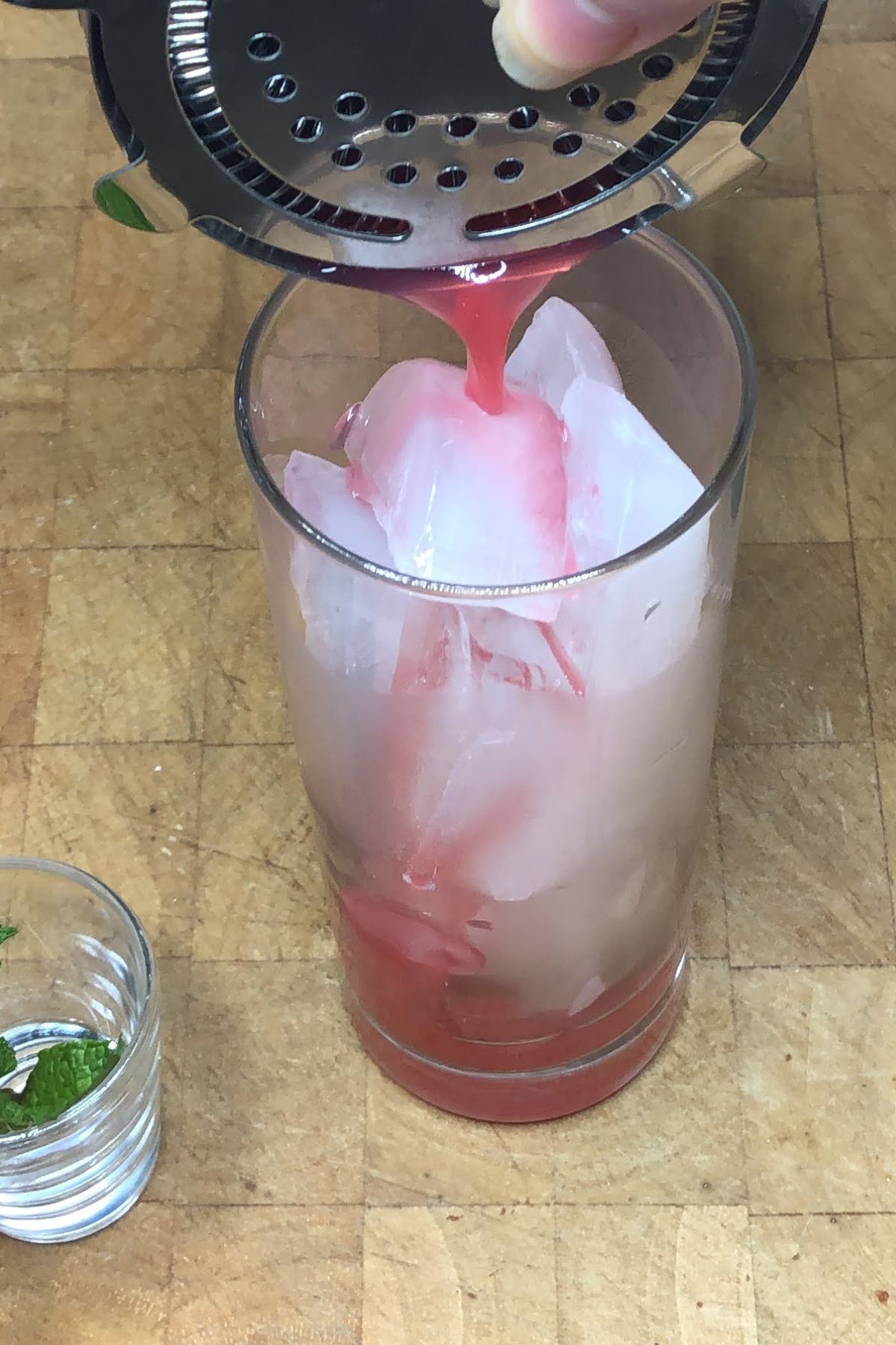 Pouring strawberry mojito mocktail from a shaker into a glass