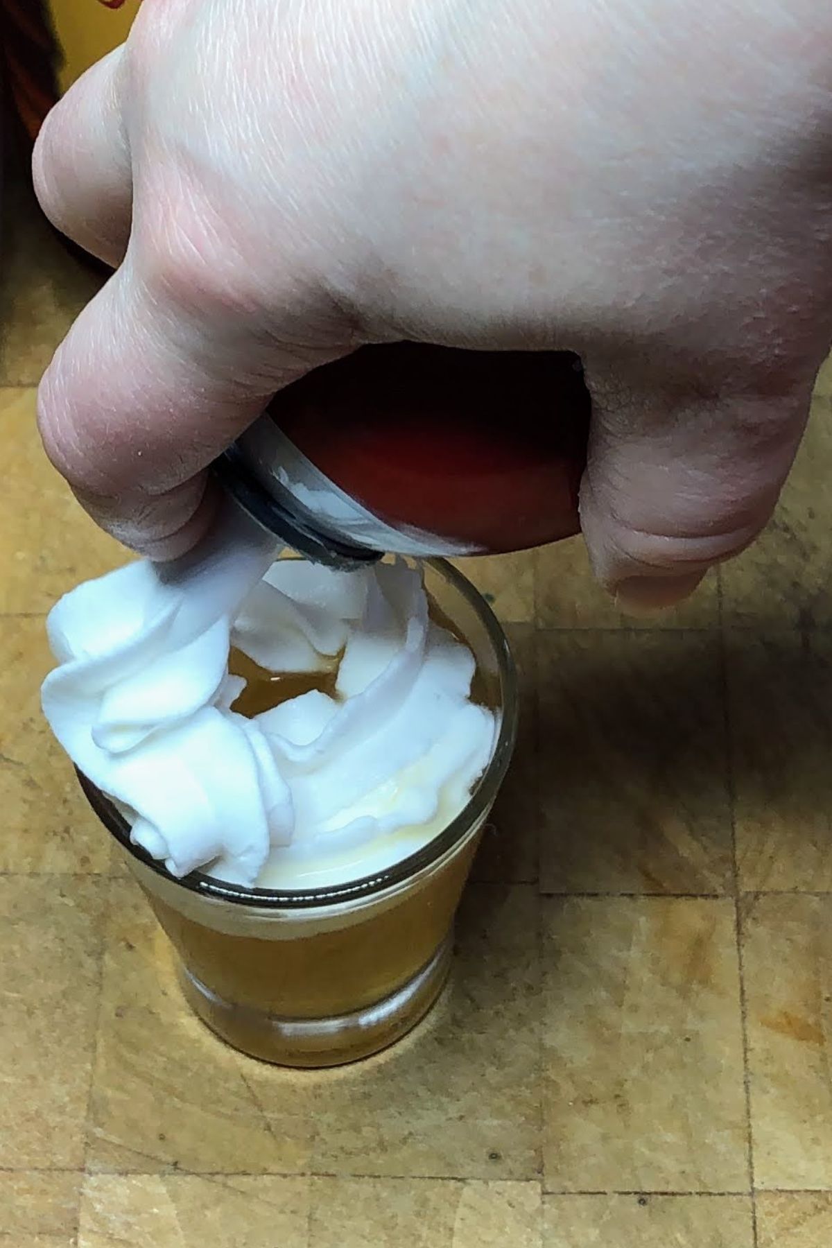 Adding whipped cream to the top of an apple pie shot.