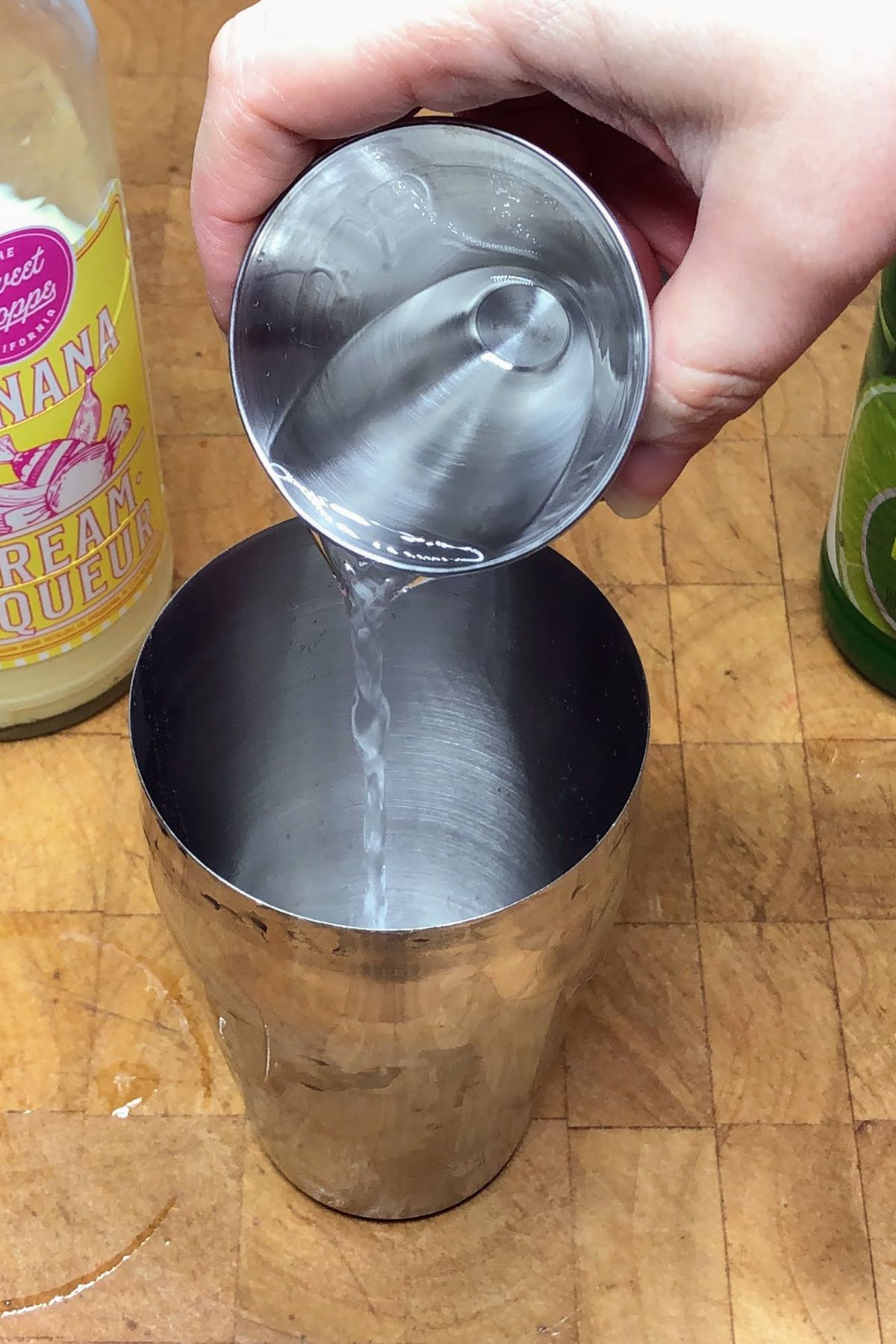 Pouring tequila from a jigger into a cocktail shaker.