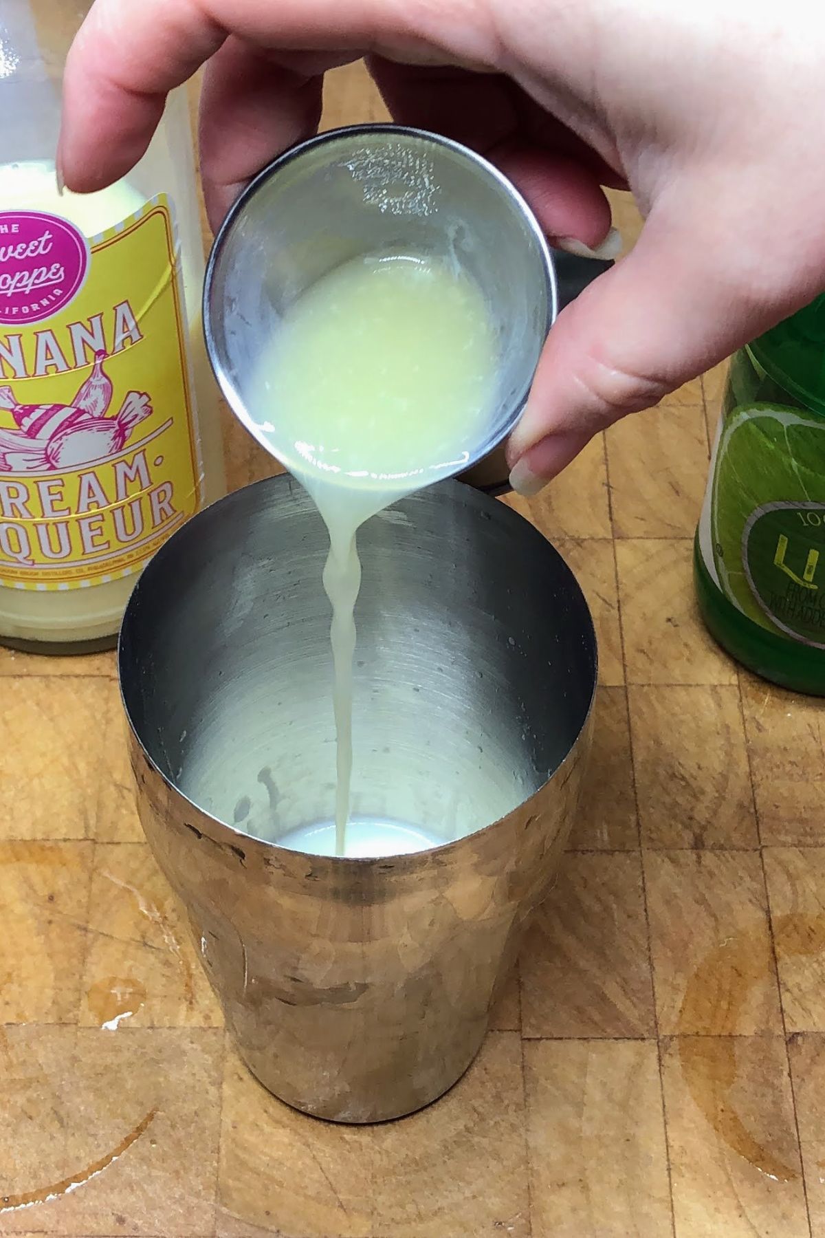 Pouring lime juice from a jigger into a cocktail shaker.