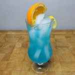 Blue Lagoon Mocktail with an orange slice in the glass on a wooden table.