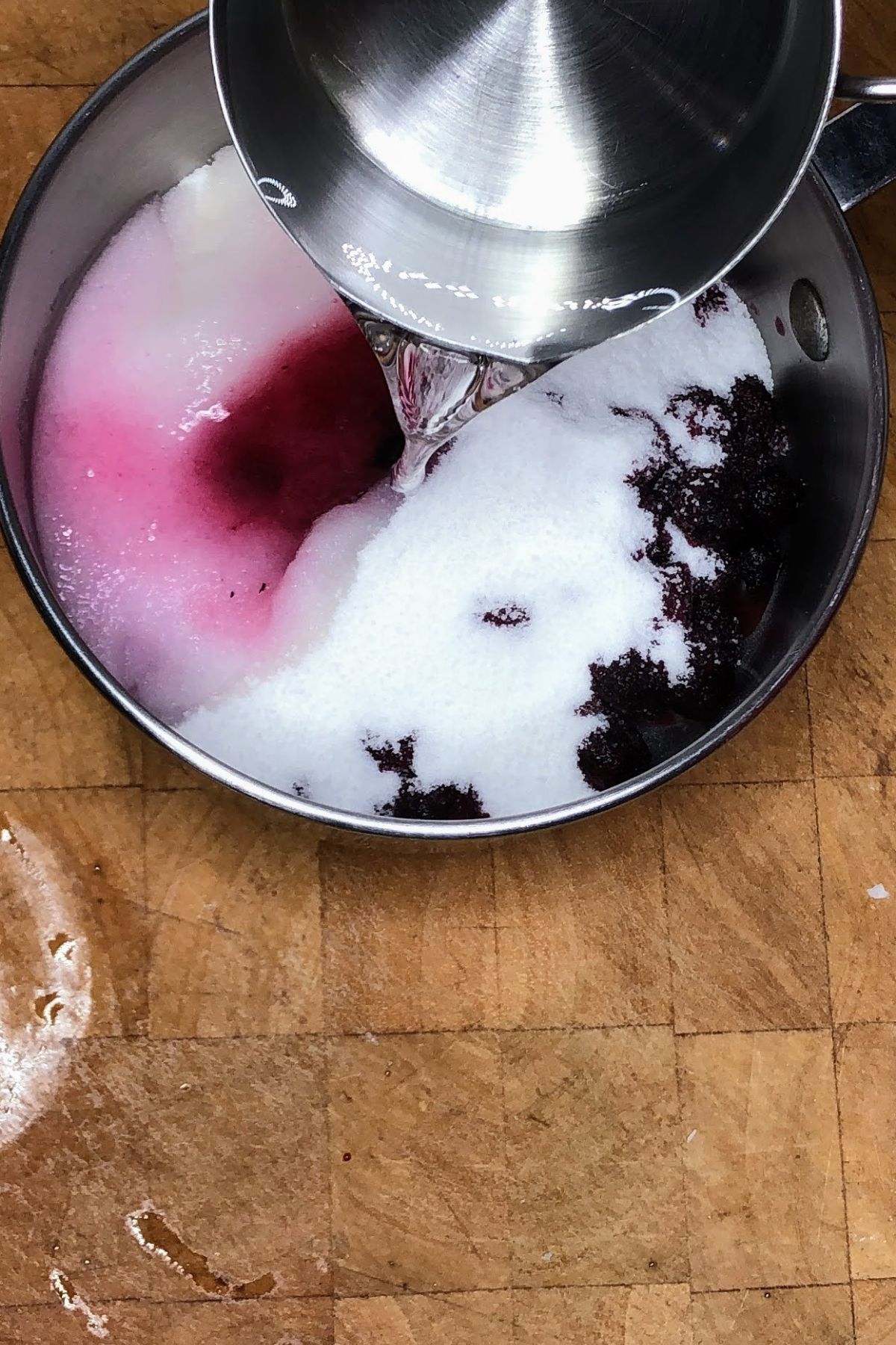 Pouring water into a pot with sugar and blueberries.