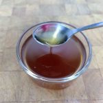 Honey simple syrup in a bowl being scooped by a spoon.
