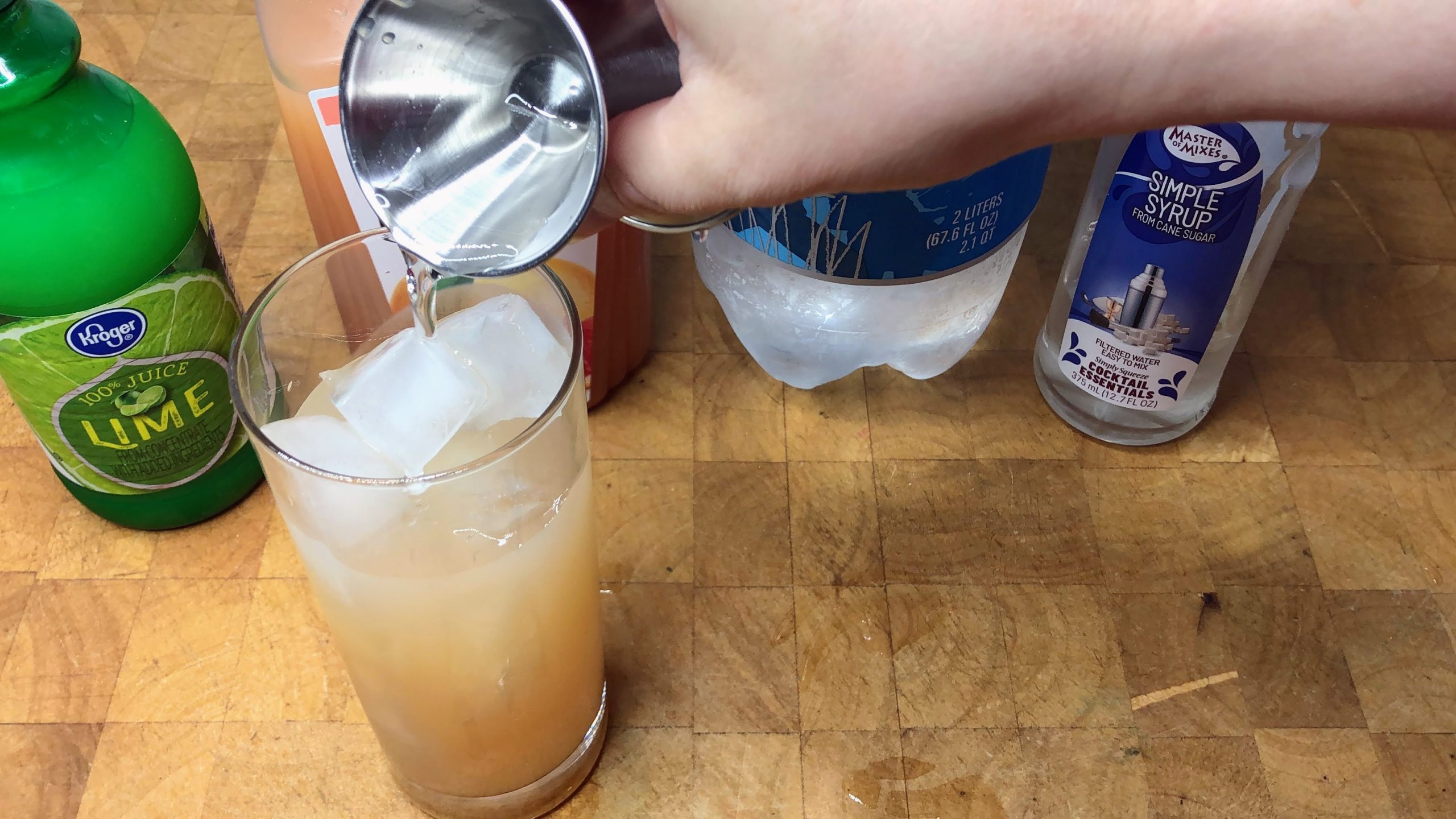 Pouring club soda from a jigger into a highball glass.