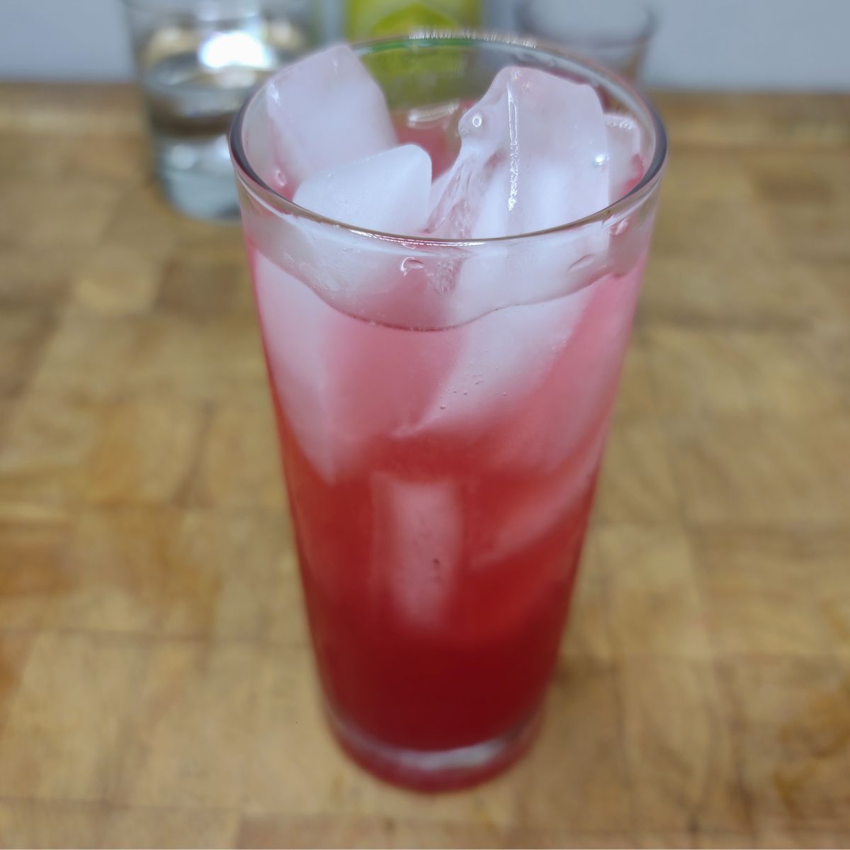 Raspberry Lemonade on a wooden table with ingredients in the background.