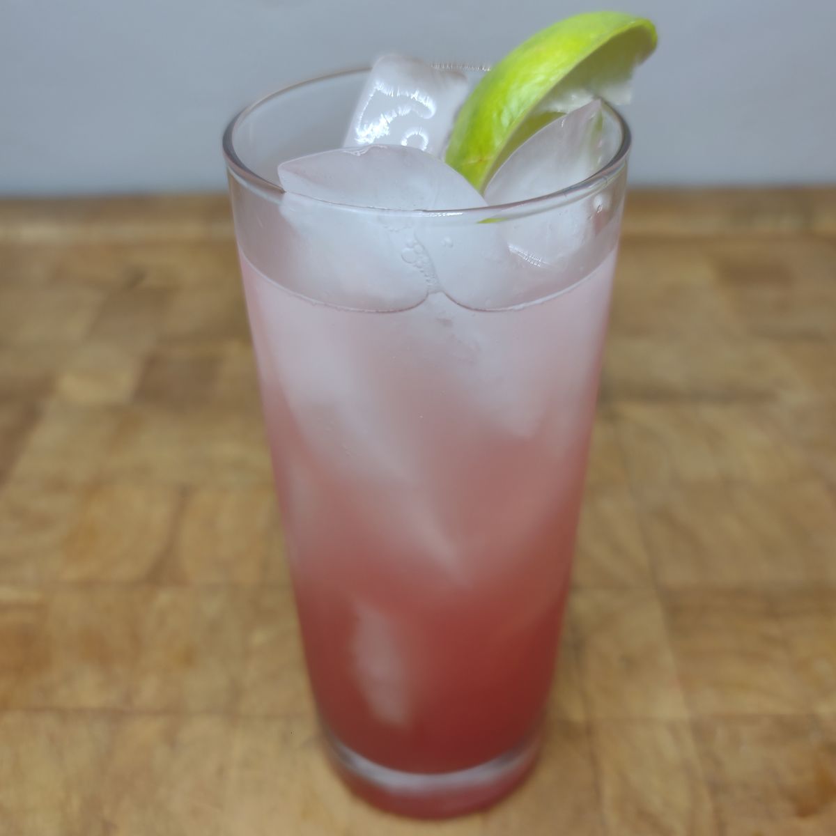 Raspberry Lime rickey with a lime wedge in the glass on a wooden table.