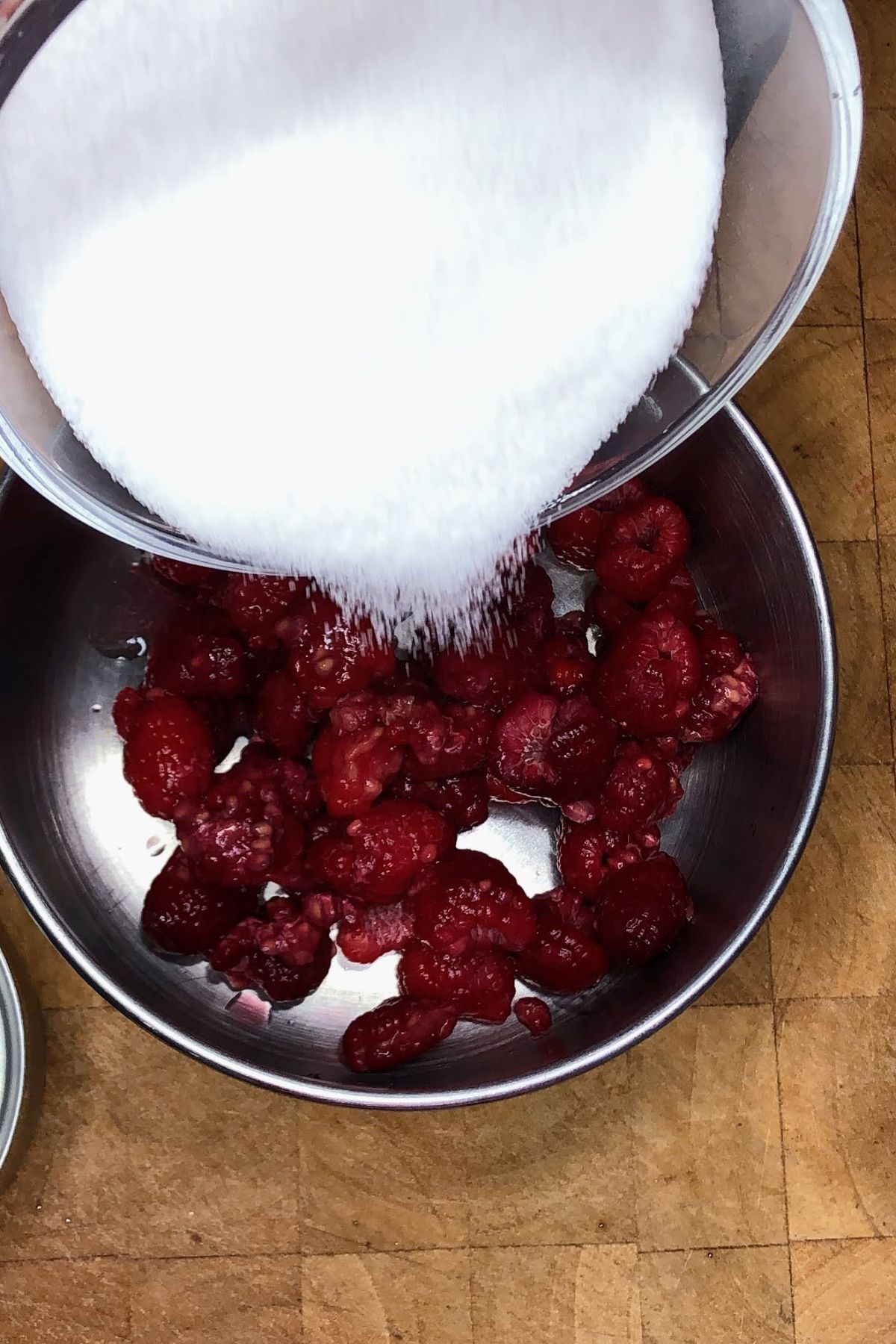 Pouring sugar into a saucepan with raspberries.