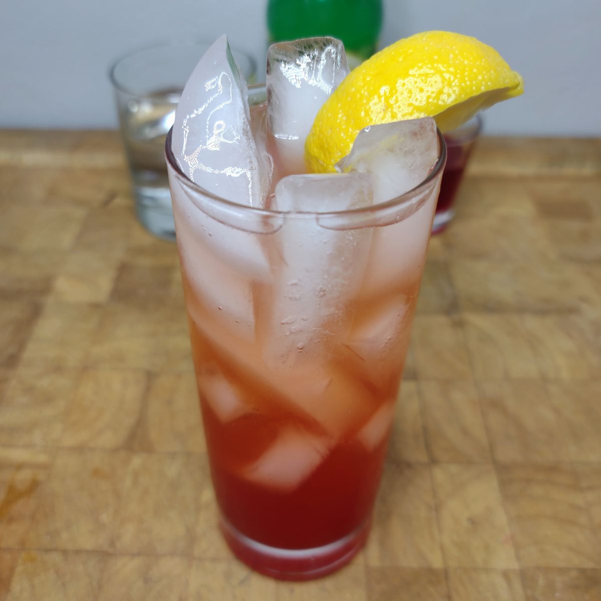 Strawberry Lemonade with a lemon wedge on the glass and ingredients in the background.