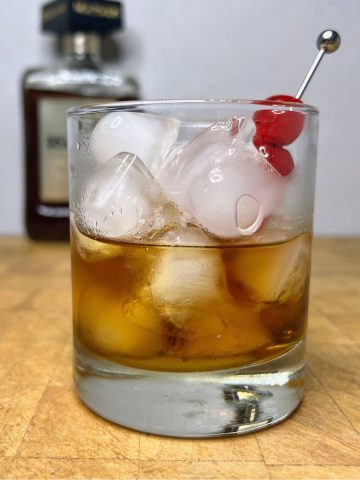 Amaretto on the rocks with cherries in the glass and bottle of amaretto in the background.