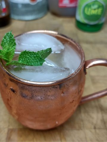 Apple cider mule on a wooden table with ingredients in the background.