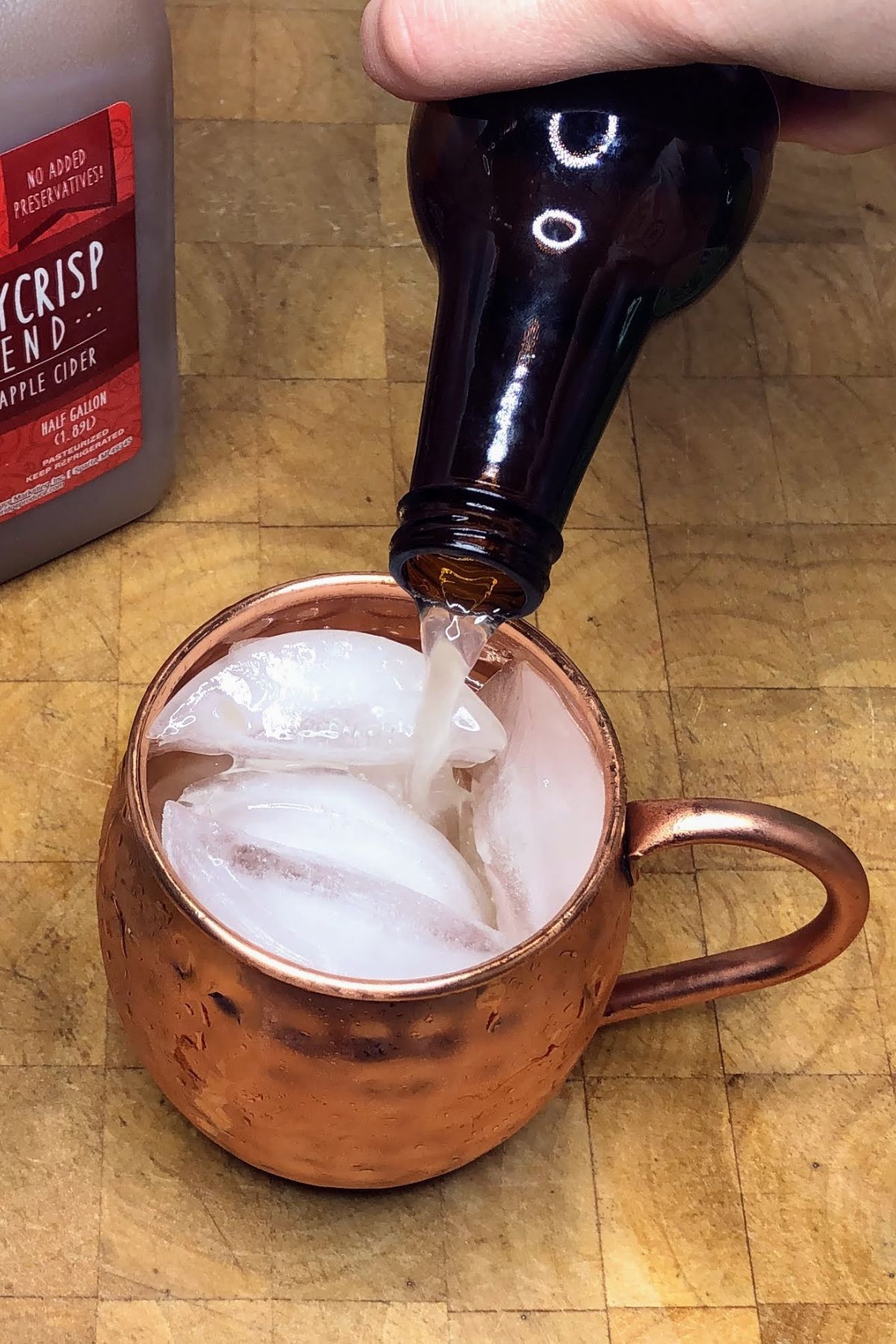 Pouring ginger beer from the bottle into a copper mug.