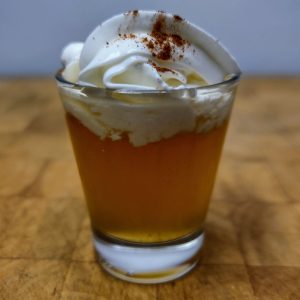 Apple pie shot with whipped cream and cinnamon on top.