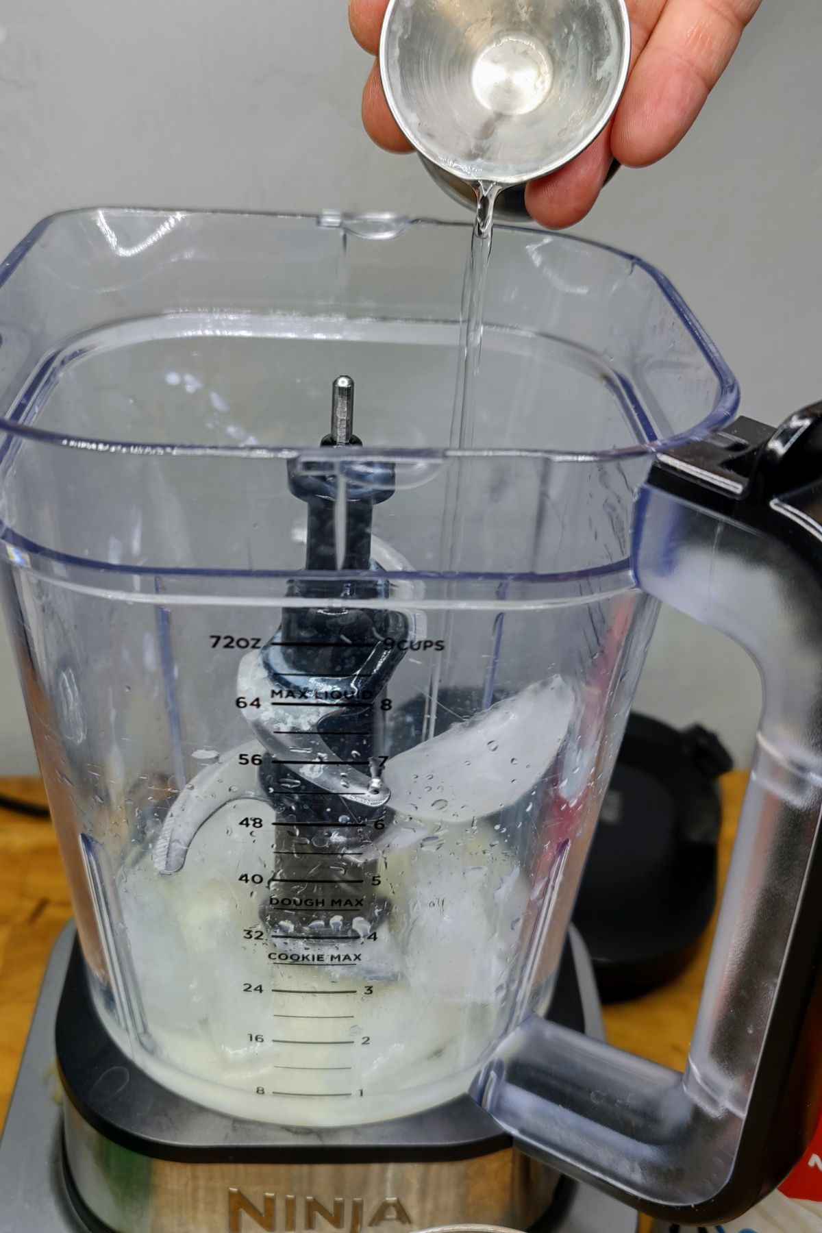 Pouring simple syrup from a jigger into a blender.